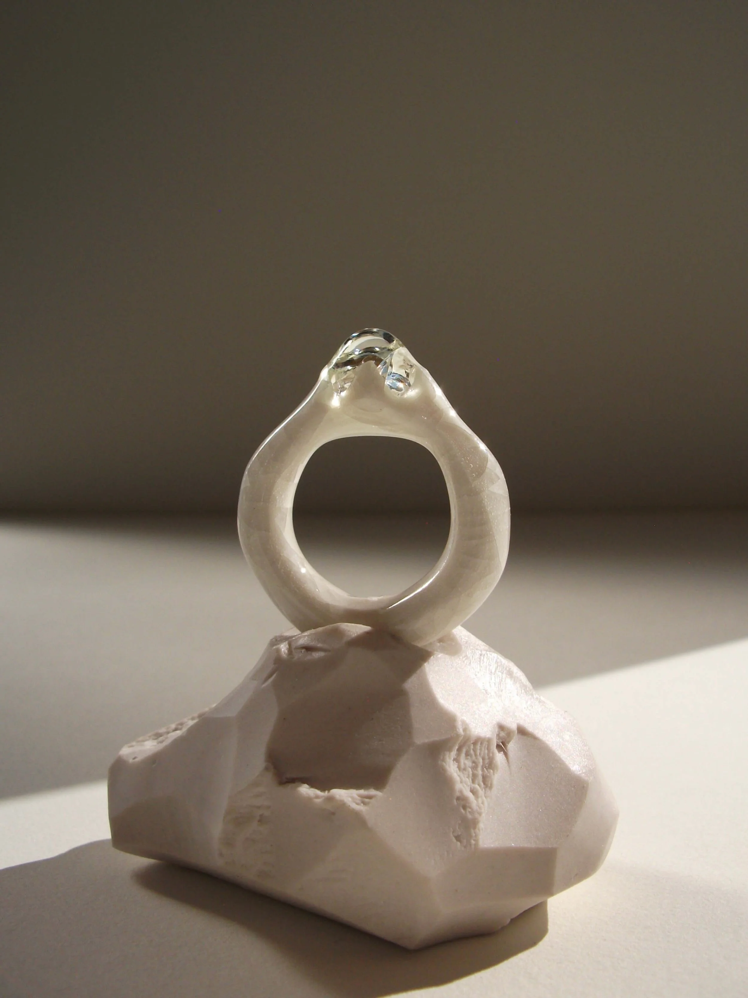 Angled view of bone-white porcelain ring with medium-wide band, crackle surface, and large glass droplet