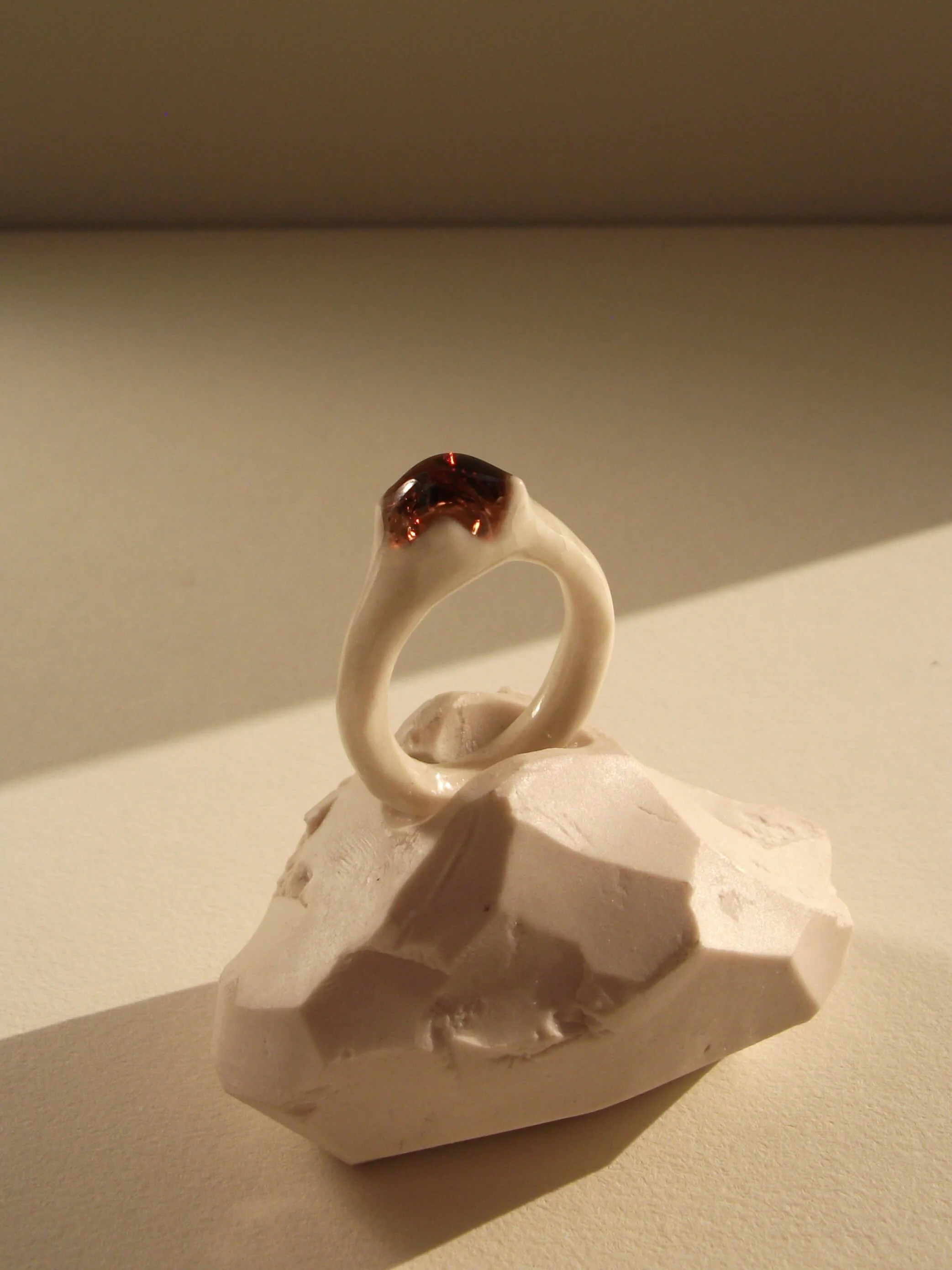Side view of bone-white porcelain ring with thin delicate band and crimson glass droplet