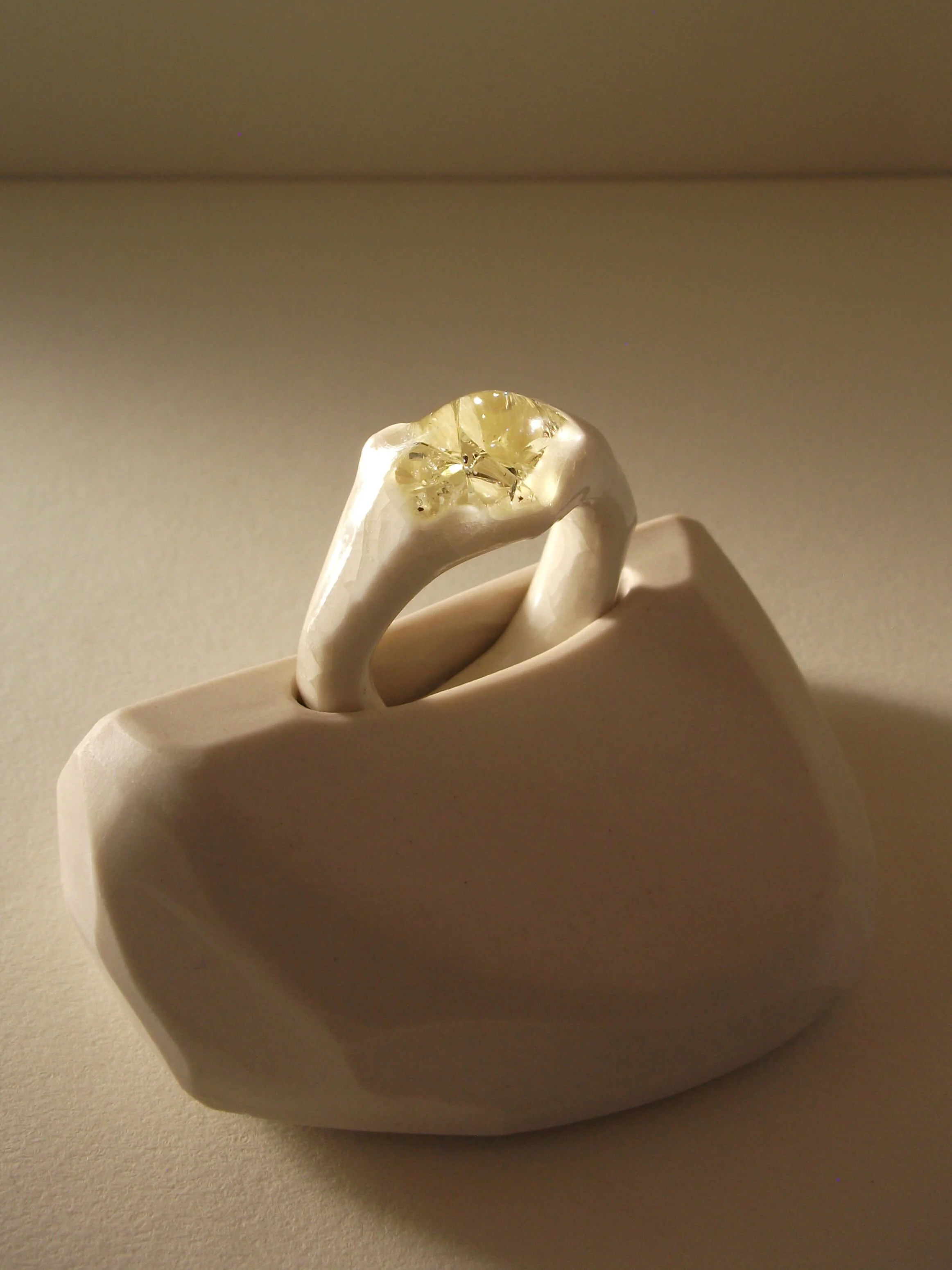 Angled view of bone-white porcelain ring with crackle surface and soft champagne glass jewel