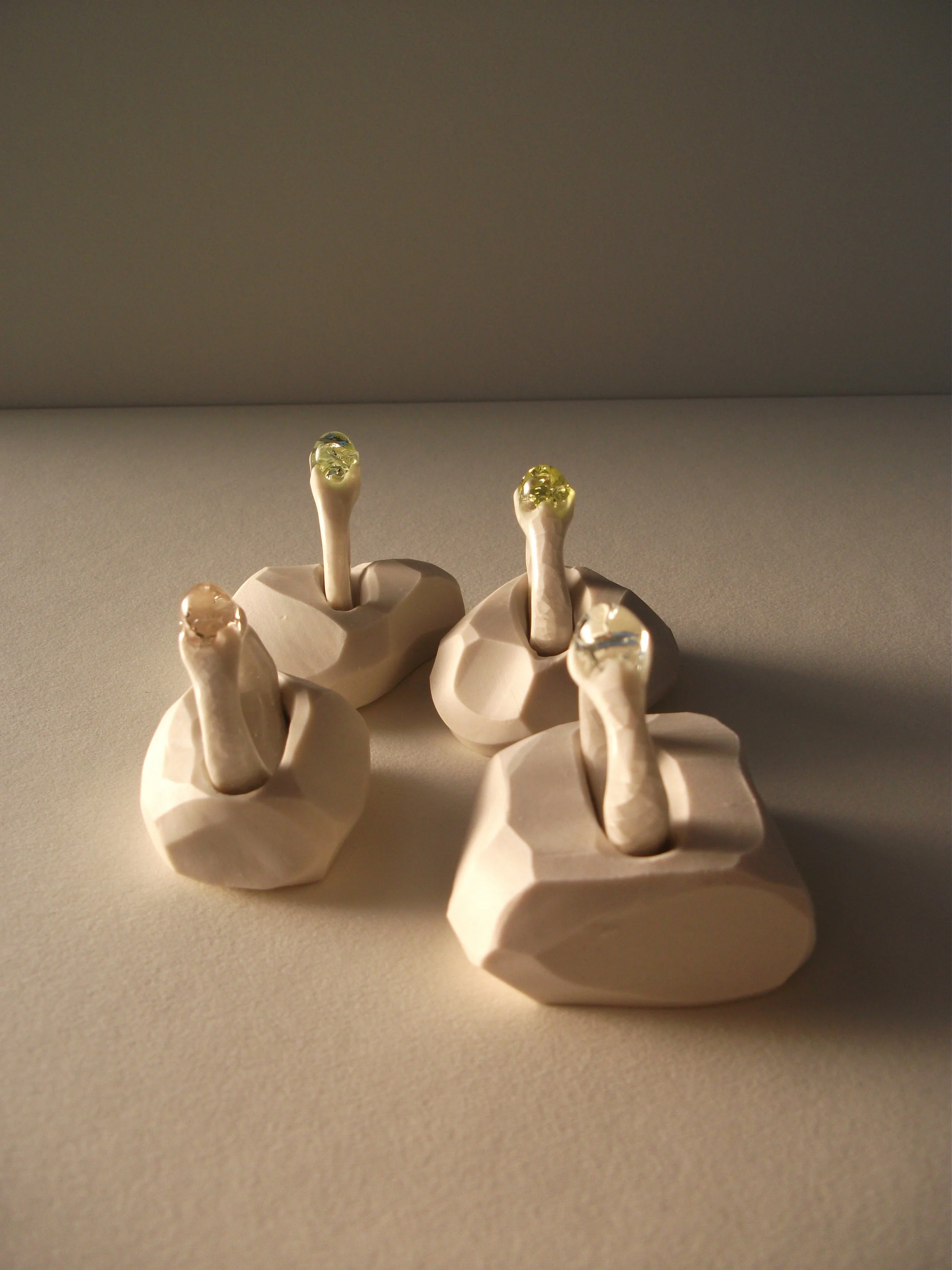 Four decorative ceramic or clay foot sculptures with gel-like material at the toes, arranged on a beige surface, lit with warm lighting.