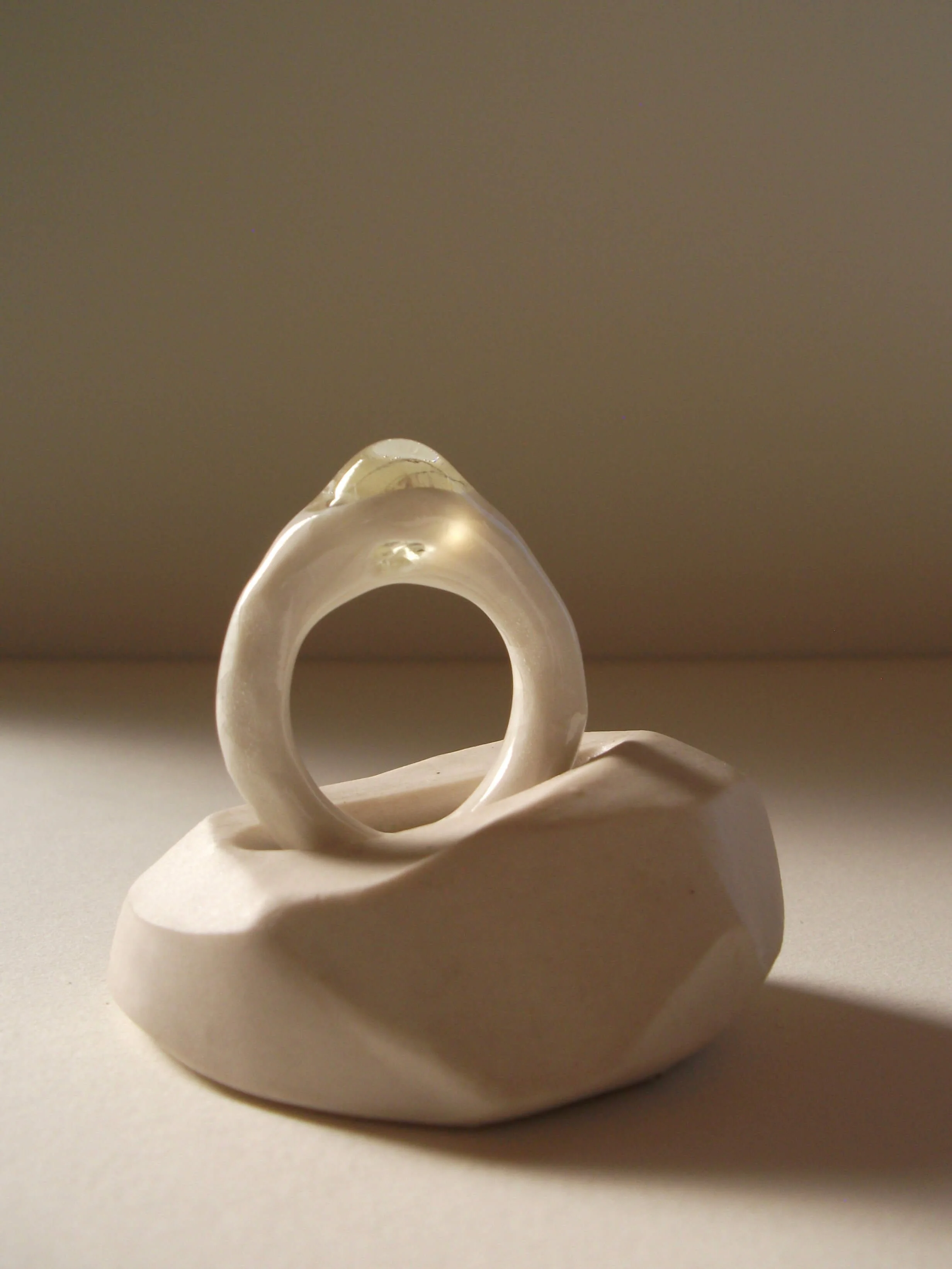 Angled view of bone-white porcelain ring with crackle surface and central glass jewel