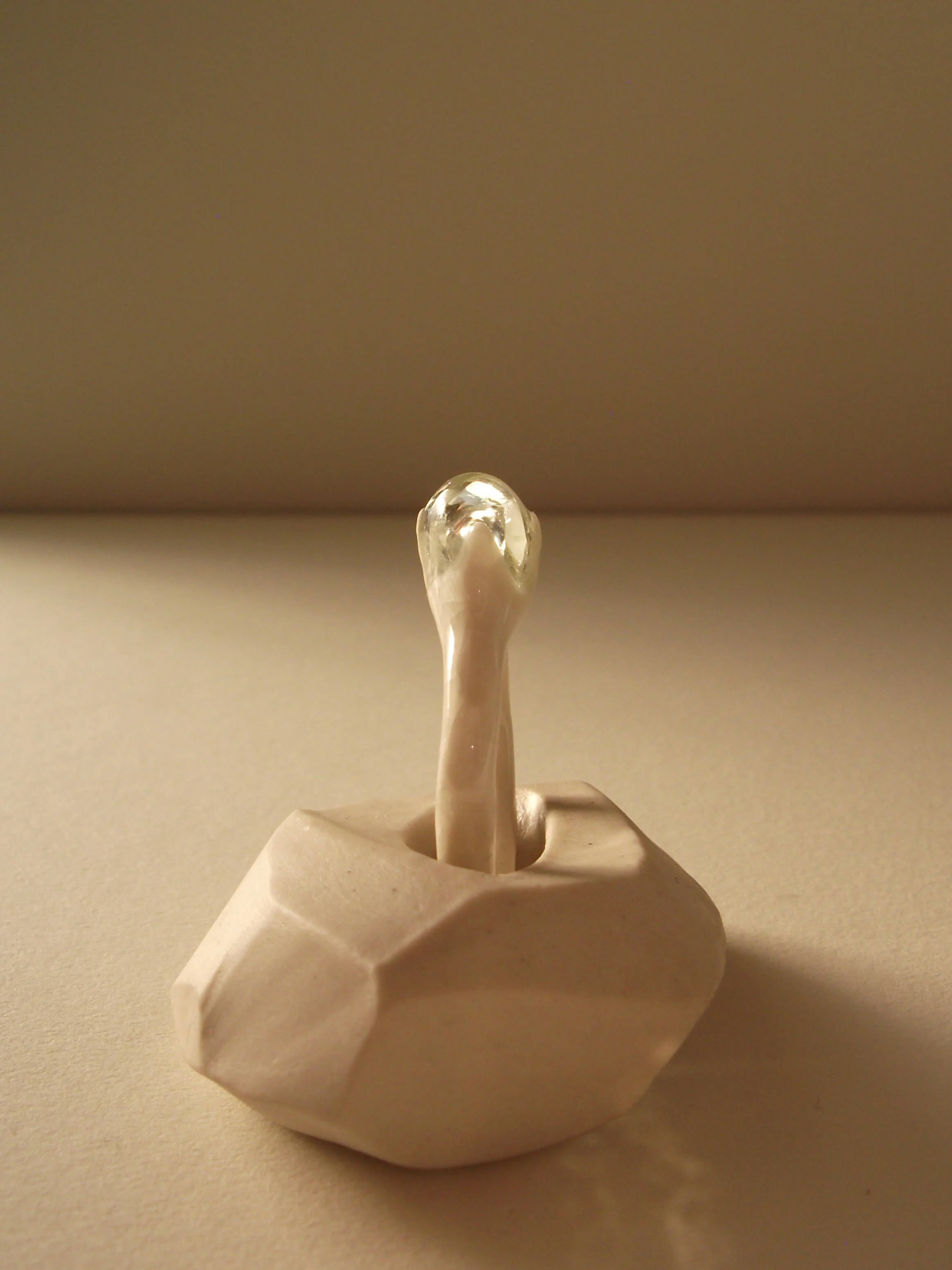 Side view of bone-white porcelain ring with thin band and single glass droplet at crown