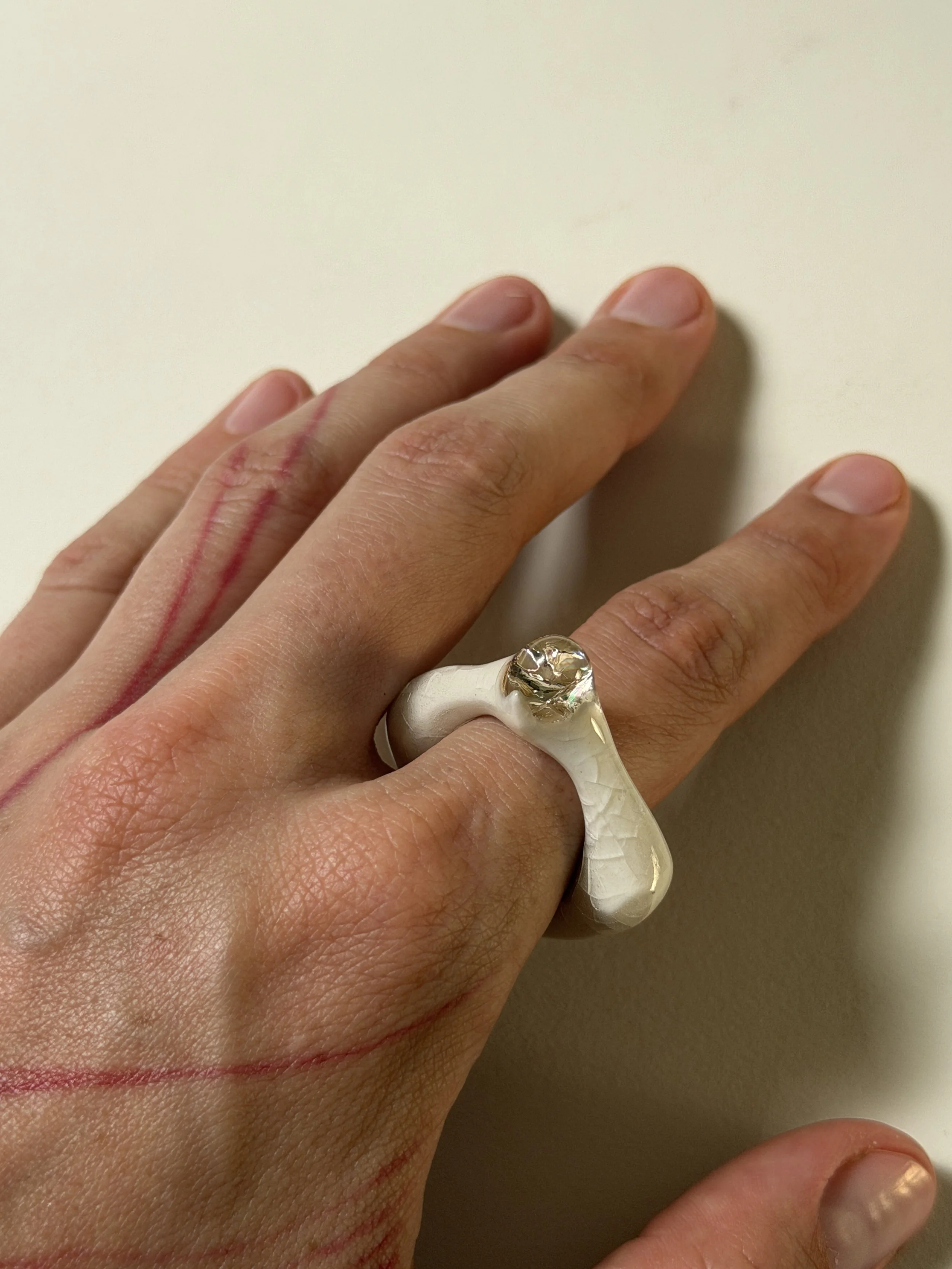 Bone-white porcelain ring worn on index finger, pale glass gemstone
