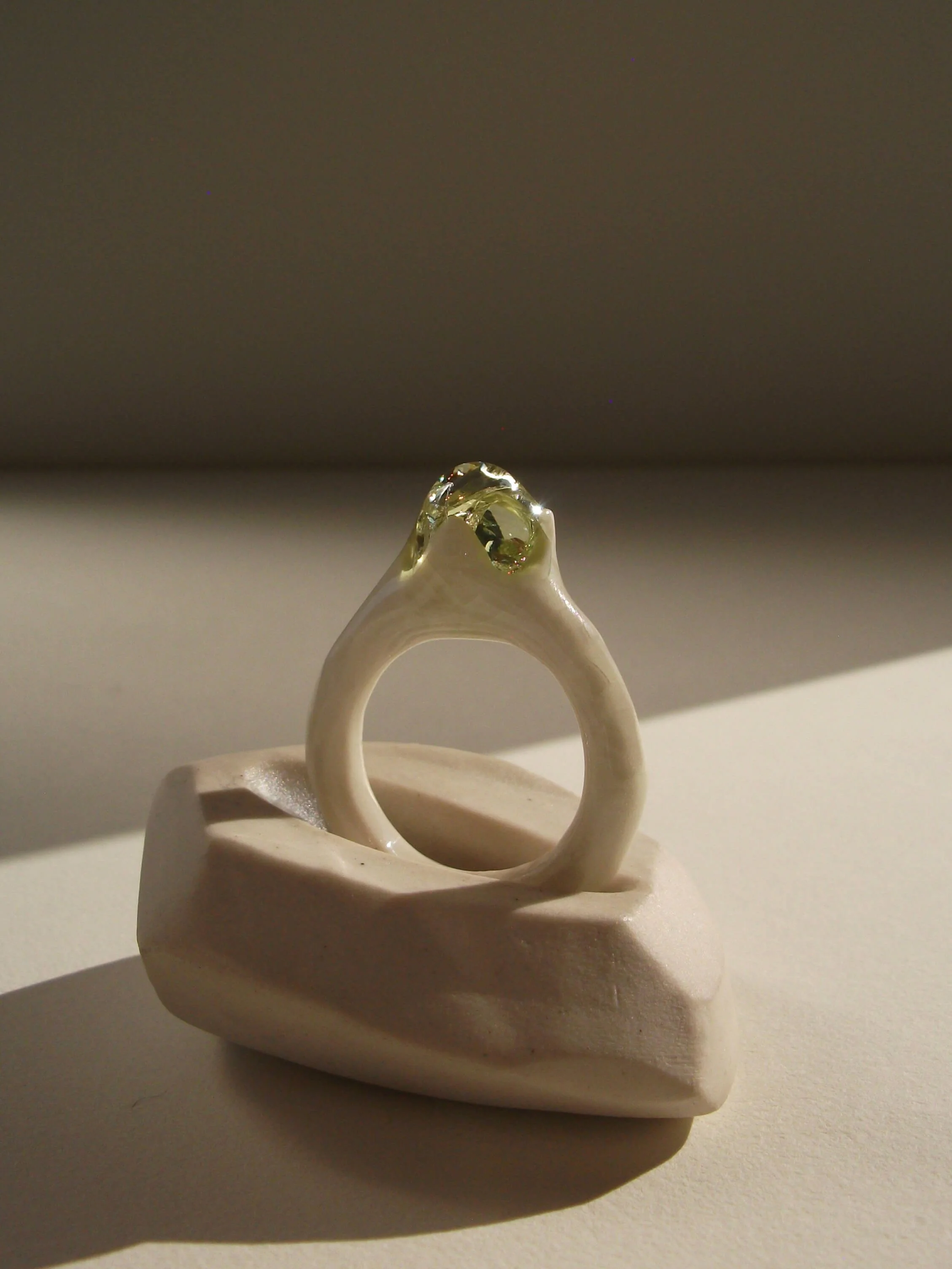Angled view of bone-white porcelain ring with thin band and glass droplet