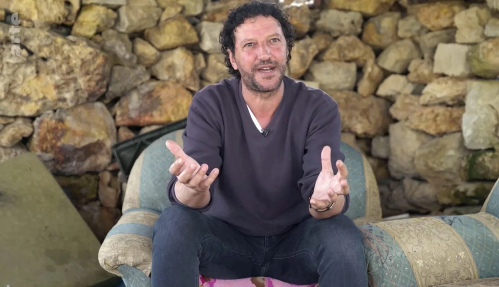 Ali Abu Awwad sitting on a chair, with arms open as if in the middle of speaking