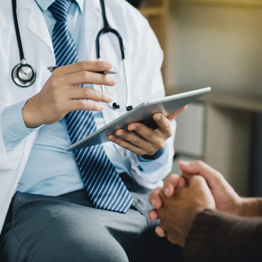 Medical professional with stethoscope holding a tablet and consulting with a patient.