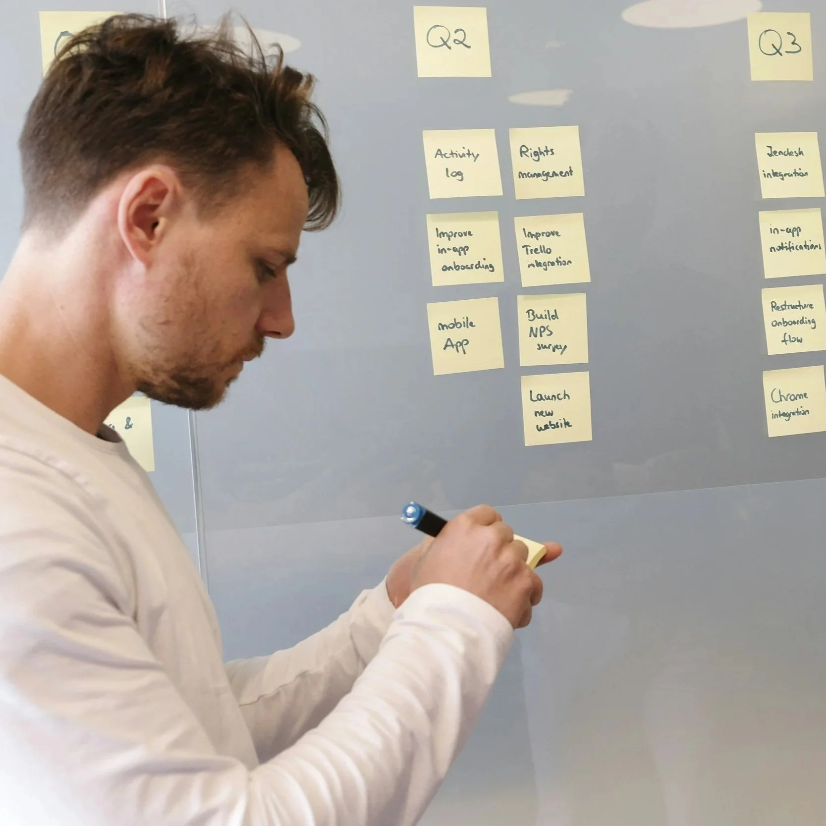 A man writing on a sticky note while standing in front of a whiteboard with organized notes on yellow sticky notes