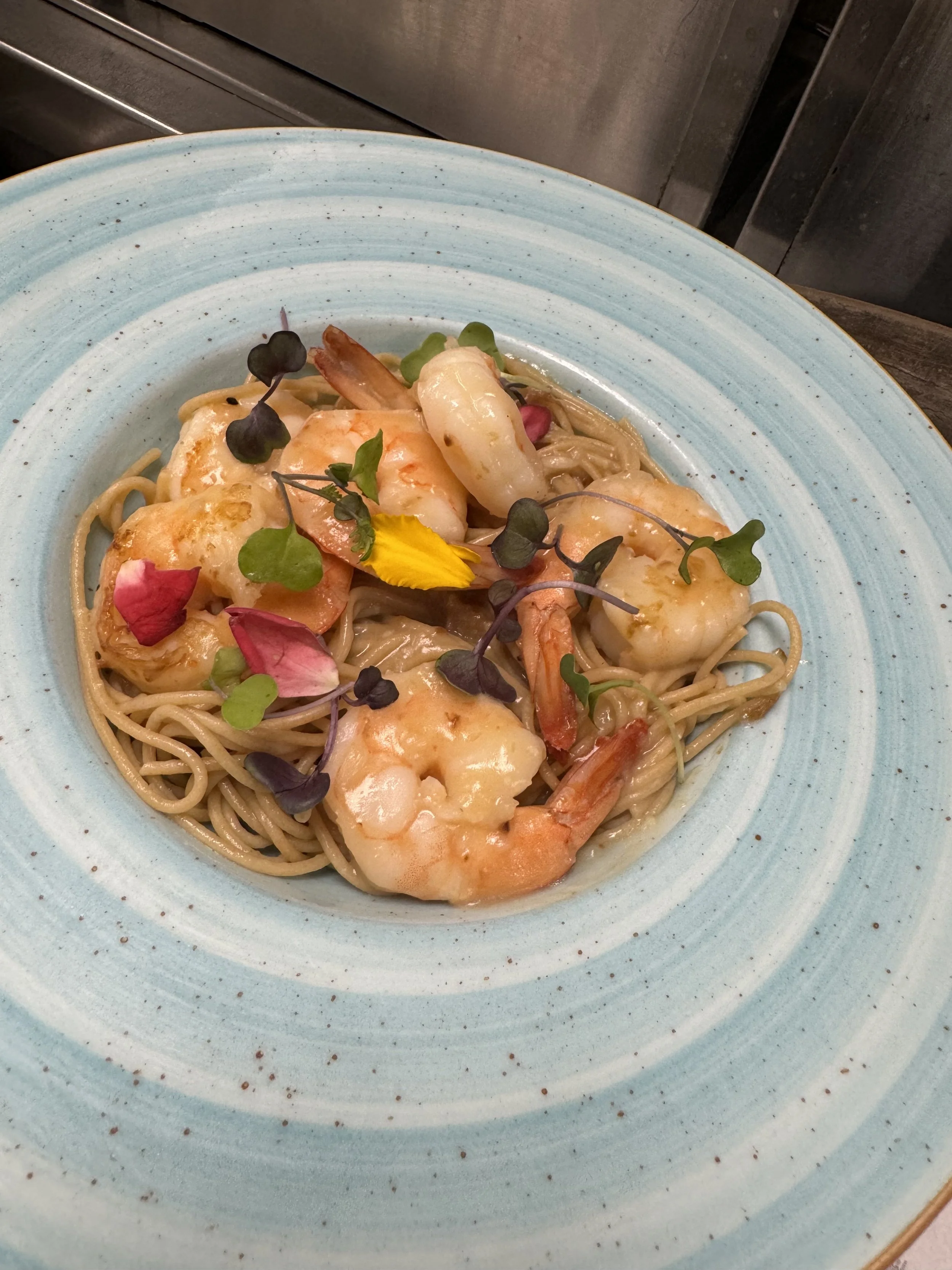 Plate of seafood pasta with shrimp, scallops, and garnished with microgreens and edible petals.