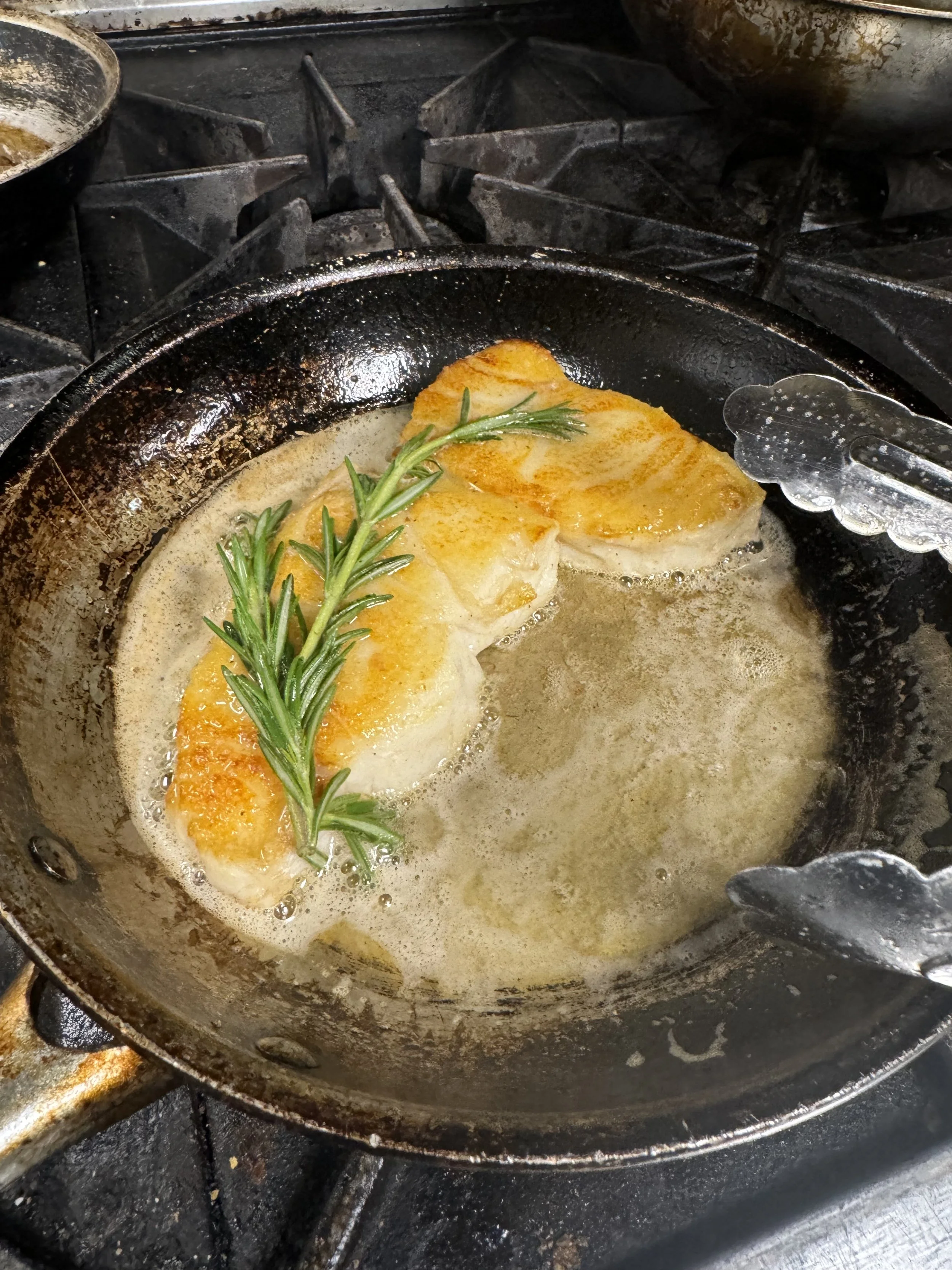 Cooking scallops in a skillet with butter and garnished with a sprig of rosemary.