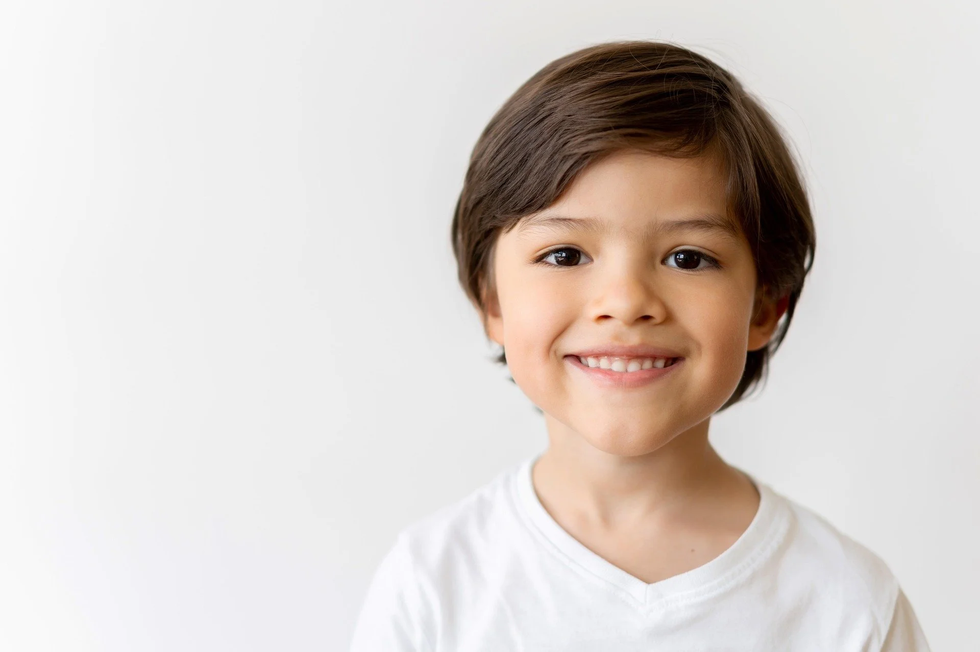 A young boy with brown hair and a white shirt smiles at the camera against a plain white background.