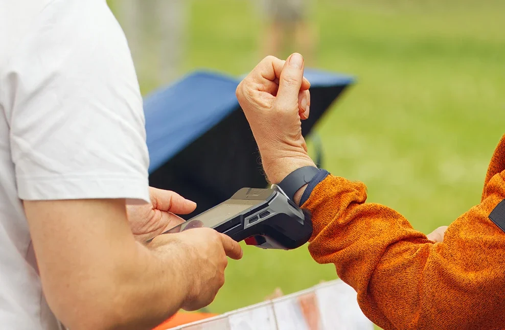 Staff member using a handheld device to scan a bracelet worn by a guest outdoors, demonstrating mobile check-in functionality.
