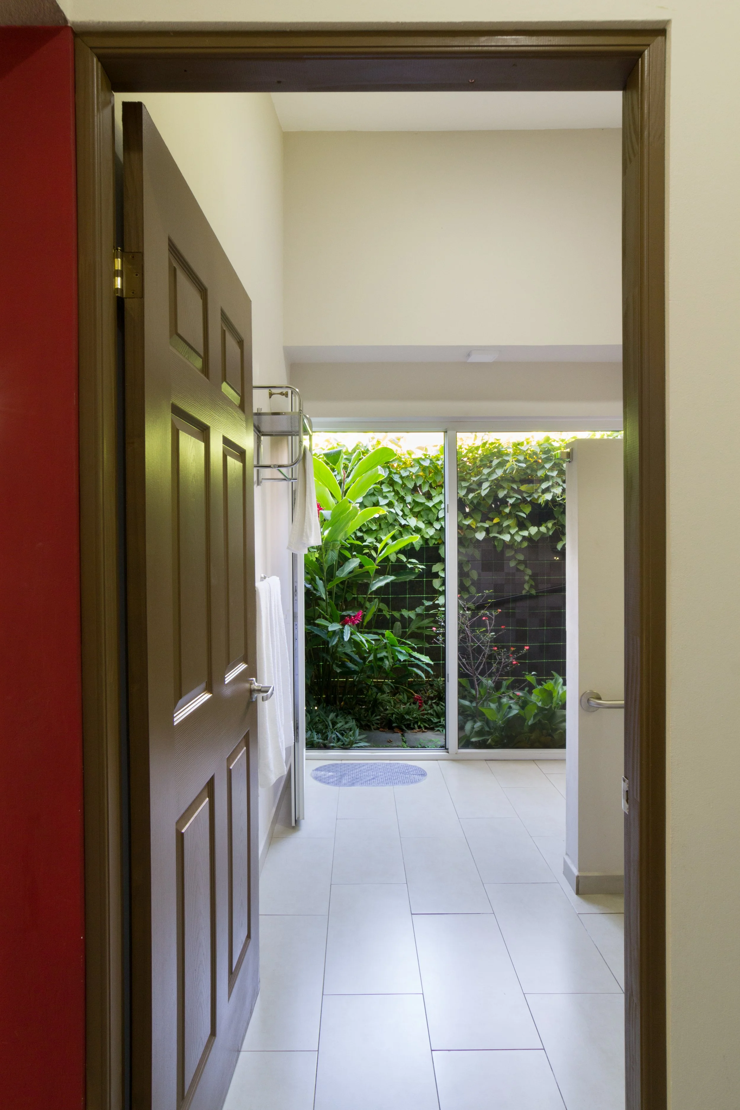 View of a bathroom door opening to a small garden area with green plants and a sliding glass door.