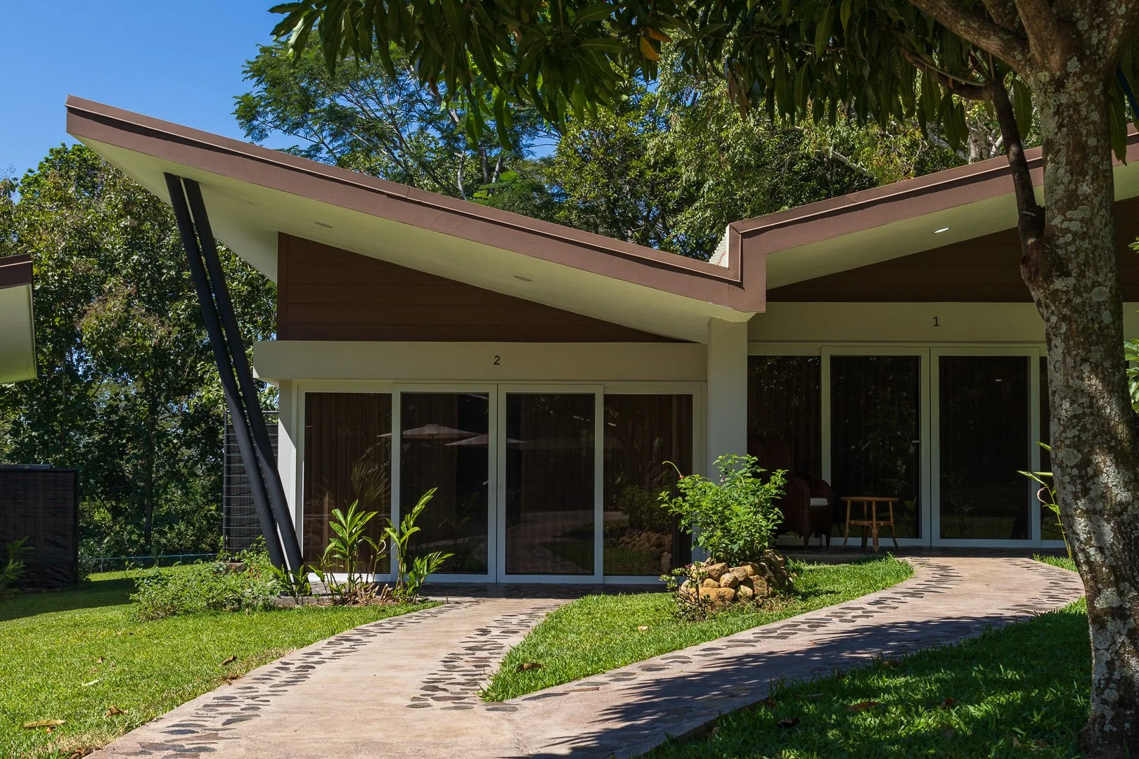 Modern house with large sliding glass doors, surrounded by greenery, with a winding pathway leading to the entrance.