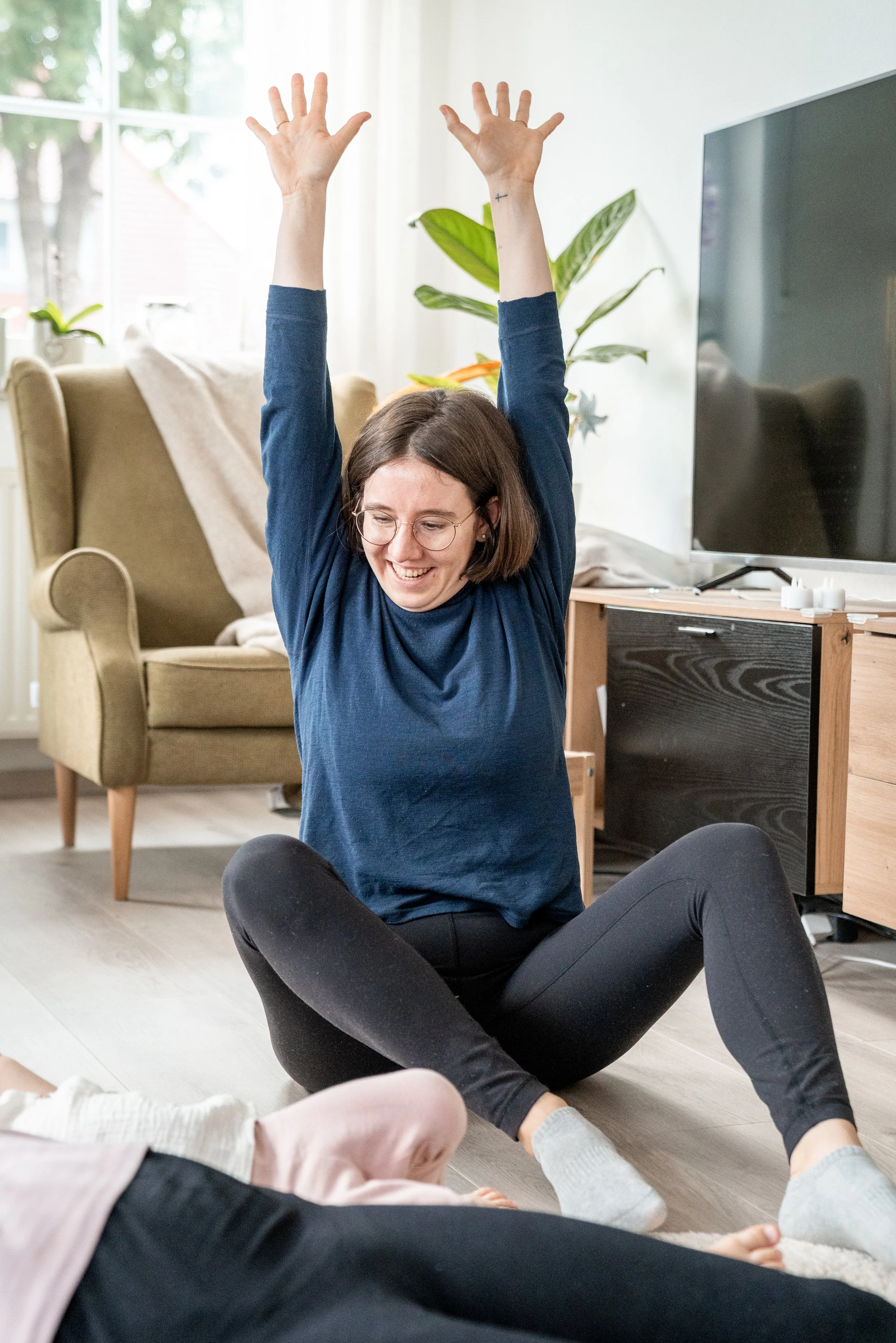 Auf diesem Bild zeige ich gerade der großen Tochter von der Mama, die ich gerade begleite, wie man sich strecken kann beim Yoga. Sie liegt dabei neben ihre Mama gekuschelt auf einer Yogamatte und wir machen gemeinsam Yoga.
