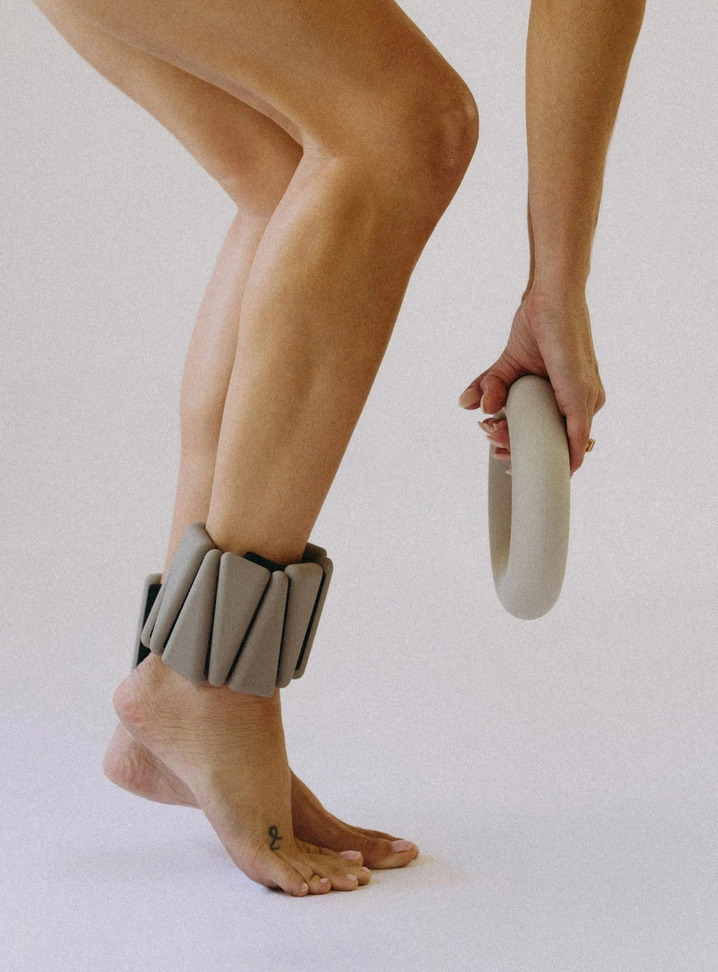 Person on hands and knees with a gray, multi-segmented ankle bracelet and holding a white ring.