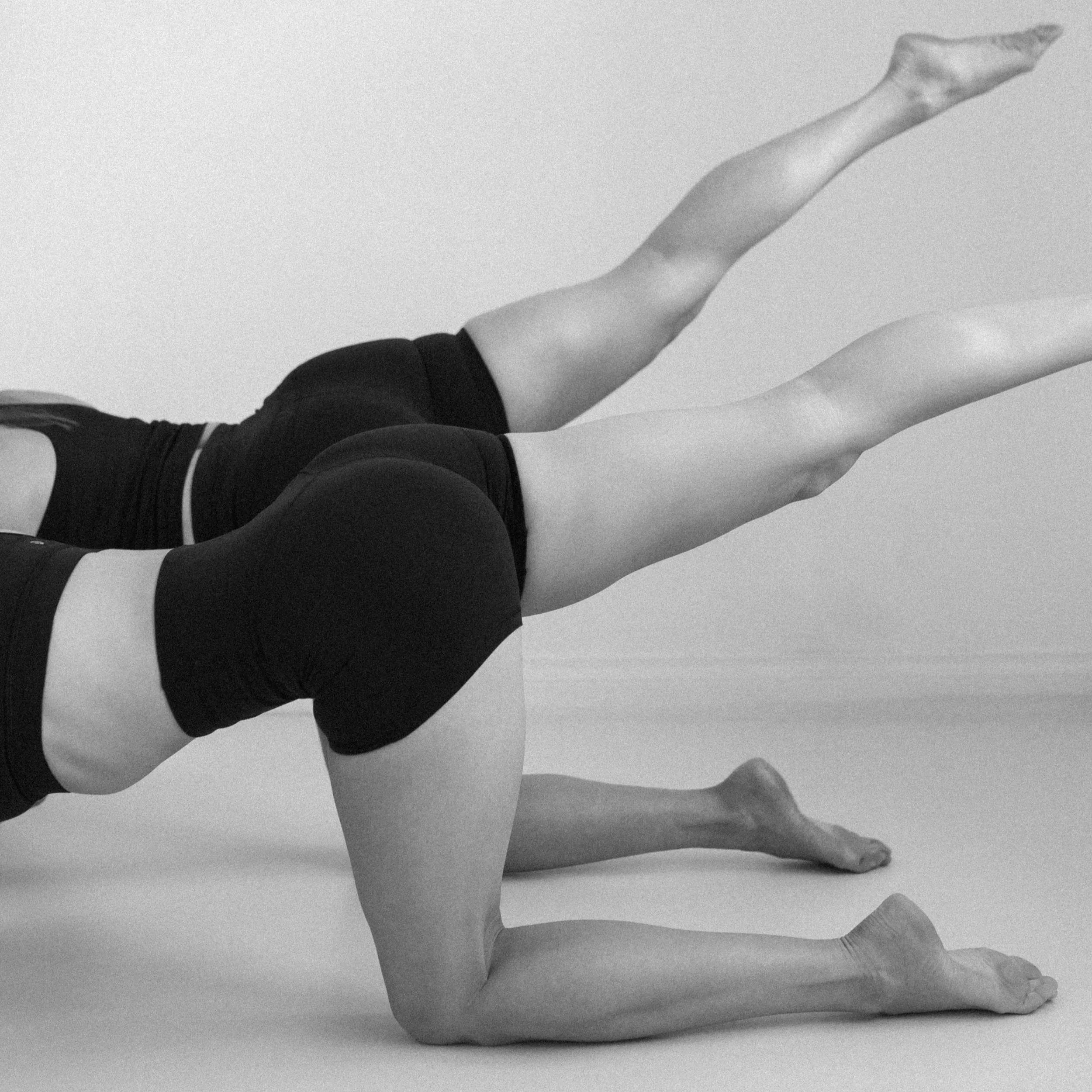 Two women in athletic clothing performing a yoga pose on the floor.