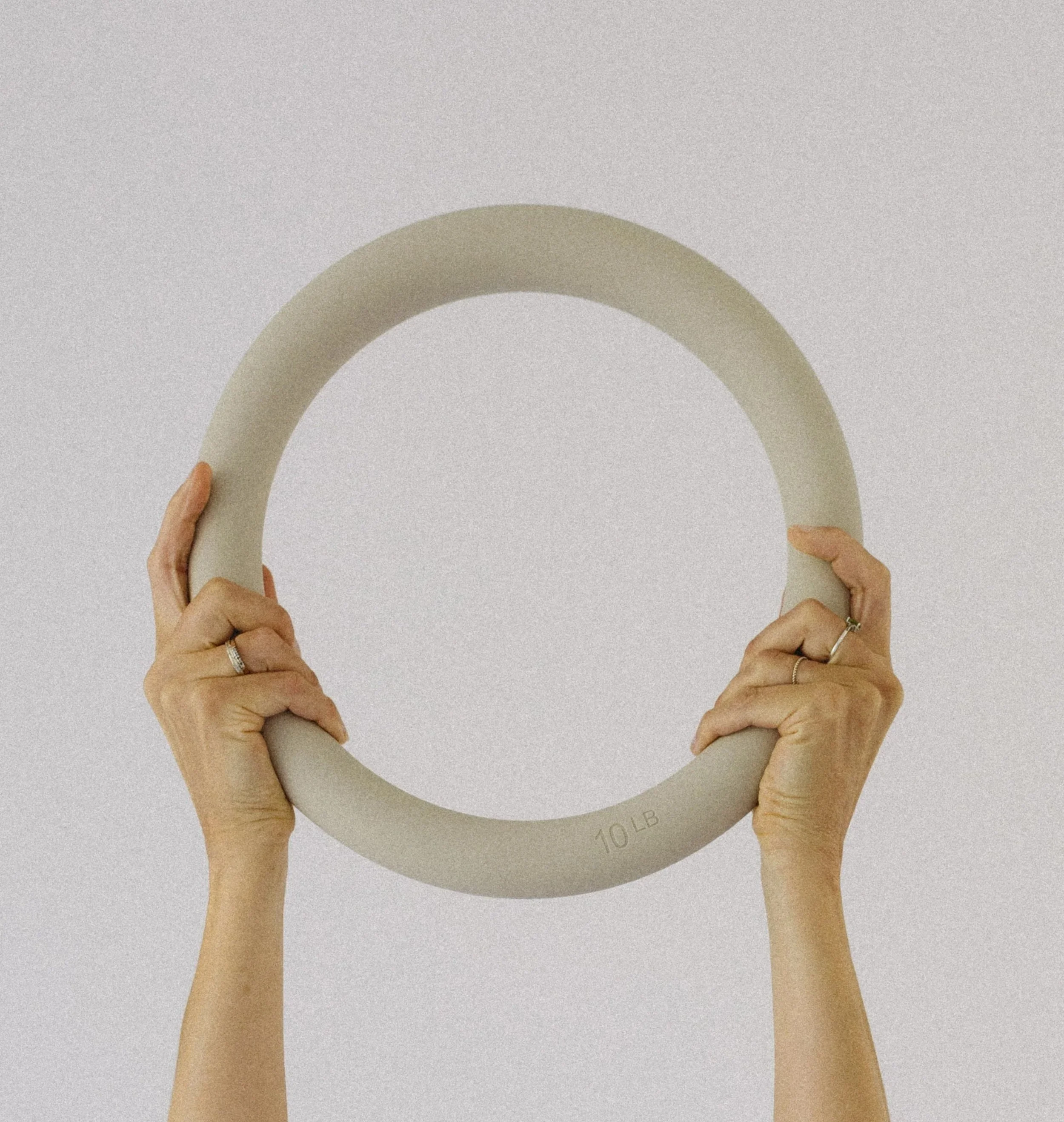Two hands holding a gray, circular weight with "10 LB" printed on it against a plain background.