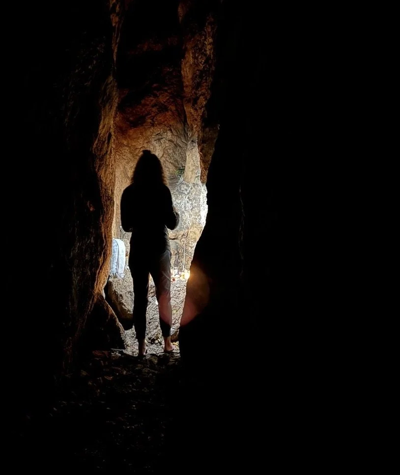 Person standing inside a dark cave, facing towards the entrance where light is coming in.