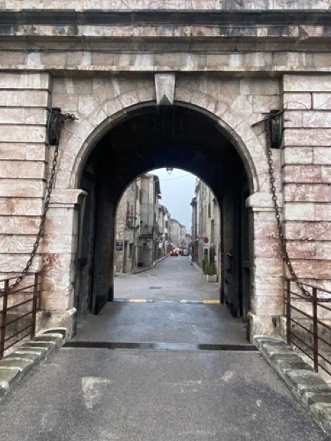Stone gate with archway leading to a street lined with old buildings.