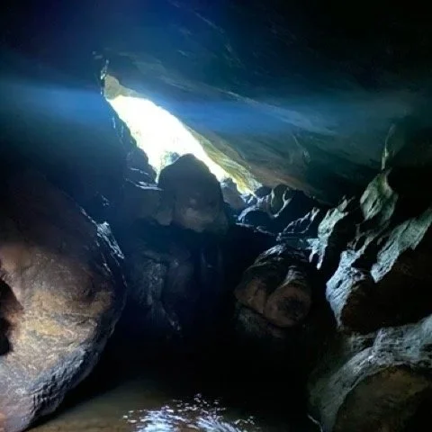 People exploring inside a dark cave with sunlight shining through an opening at the cave's entrance.