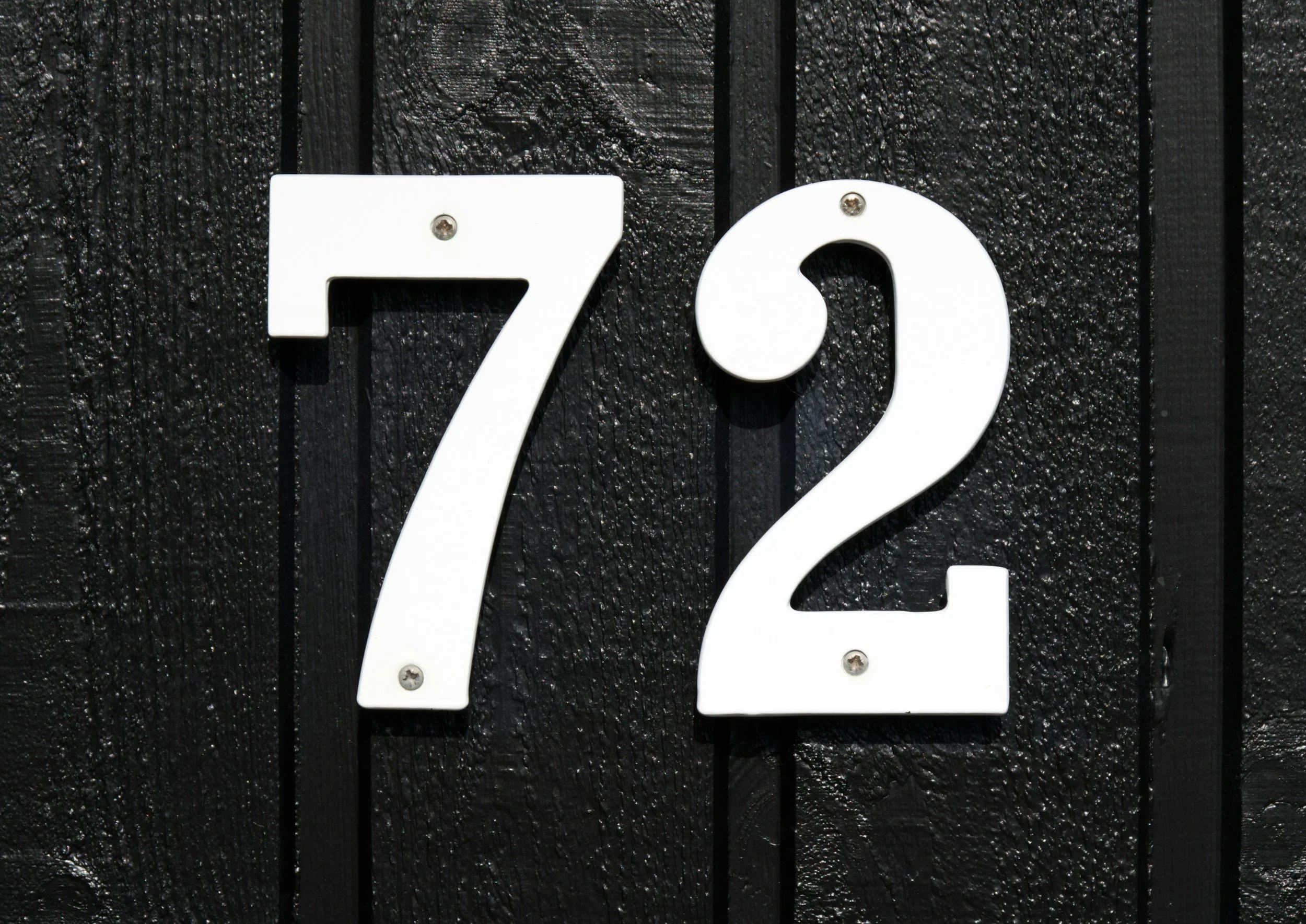 House number 72 displayed on a black wooden wall.
