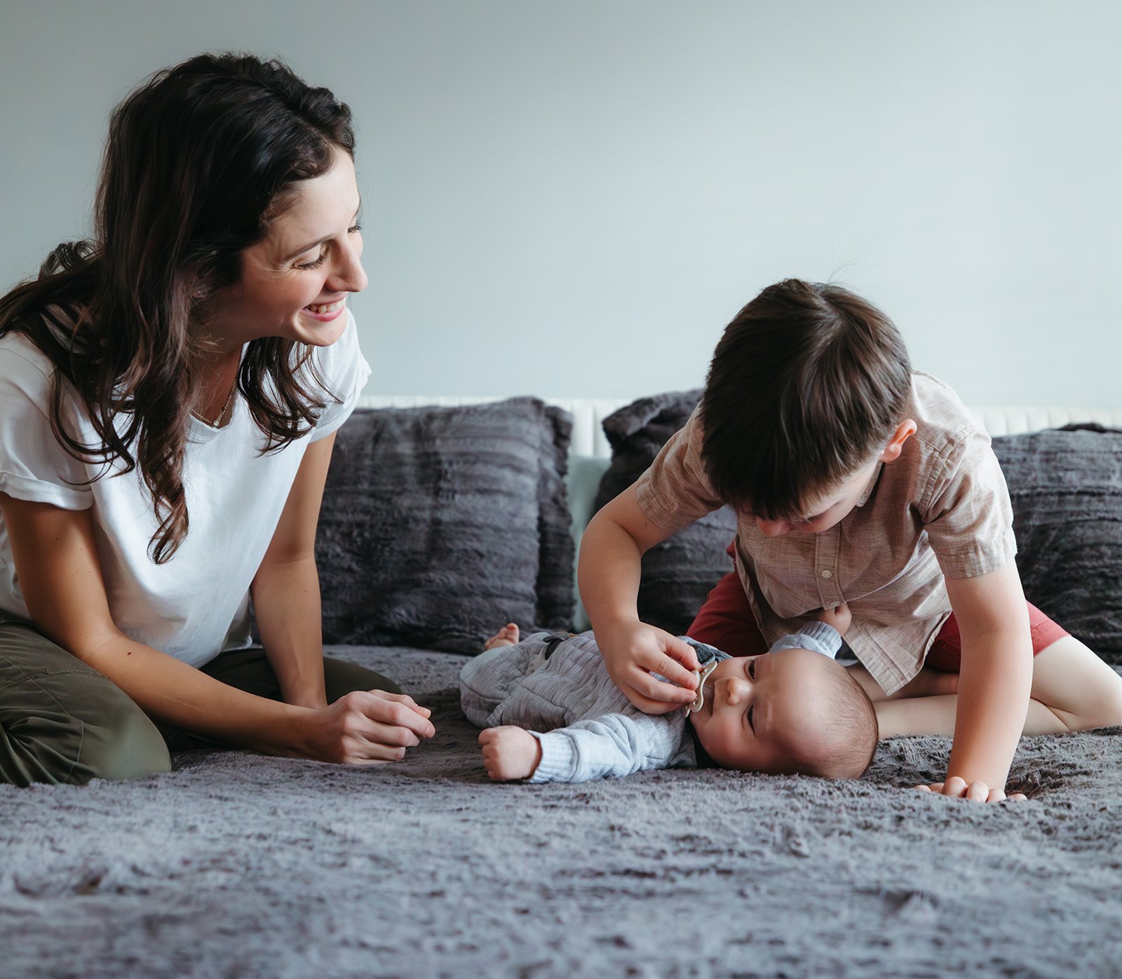 postpartum doula helping older brother play with the new baby safely
