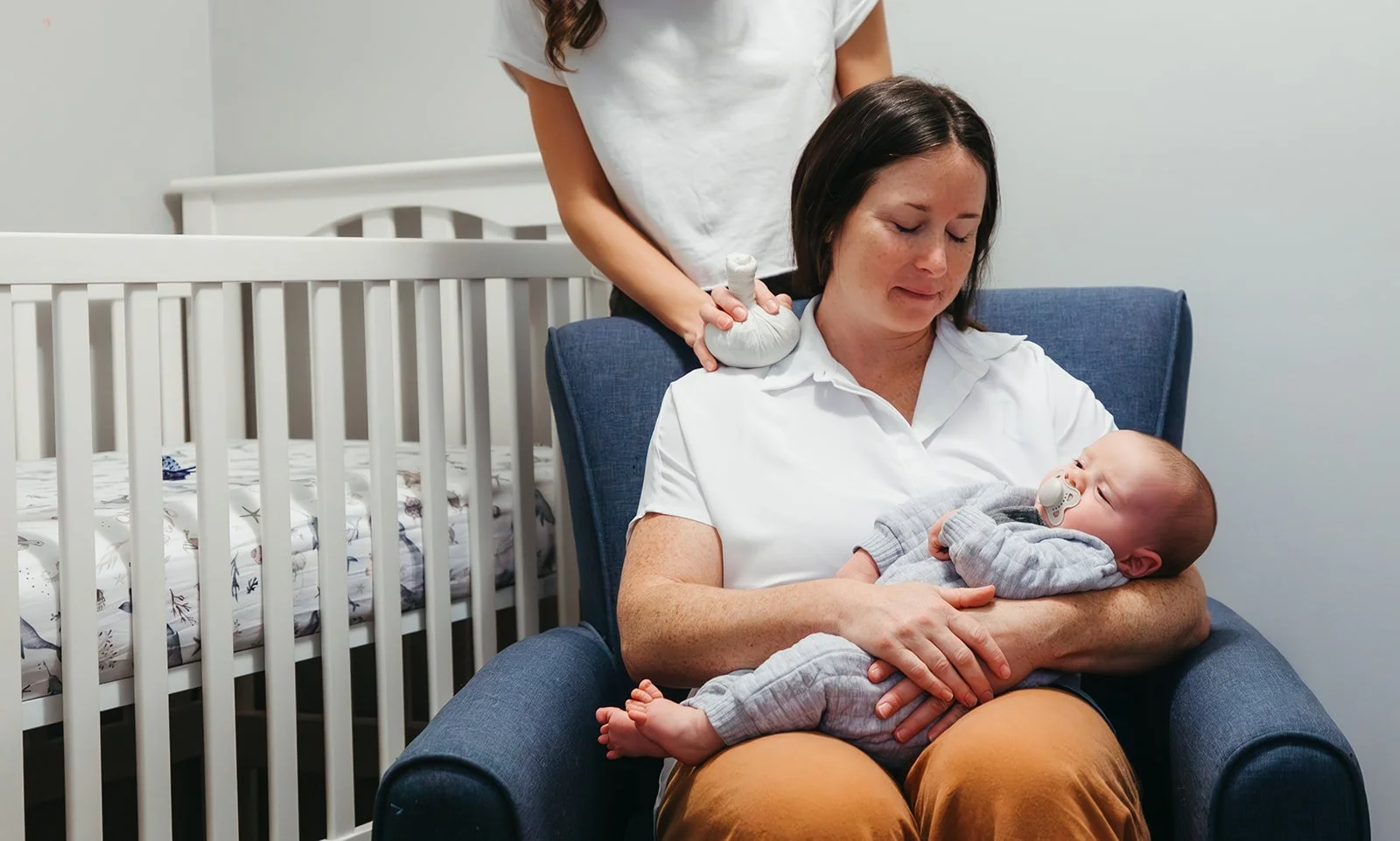 postpartum doula soothing a new mother with an herbal compress to treat her sore shoulders