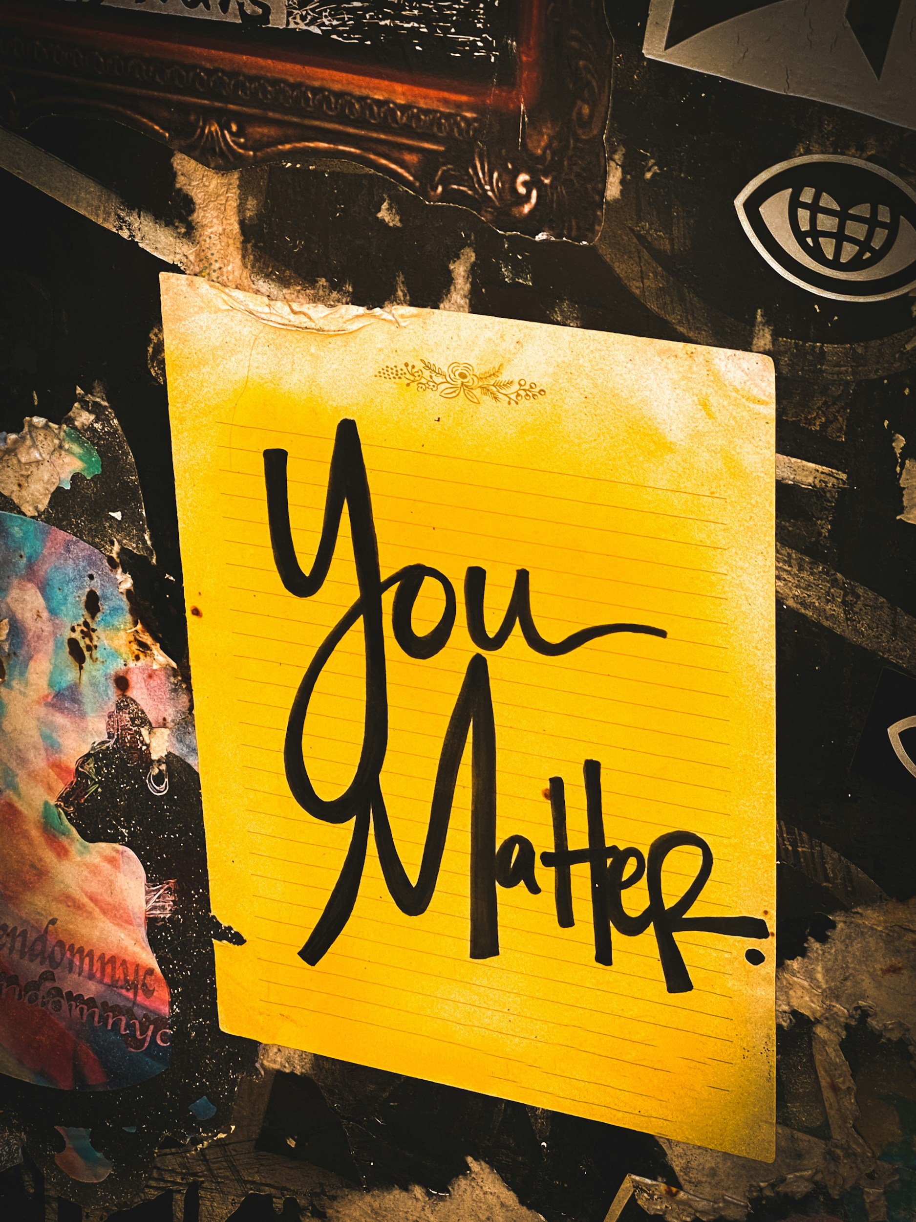 A yellow note card with the words 'You matter' written on it, surrounded by various stickers on a dark surface.