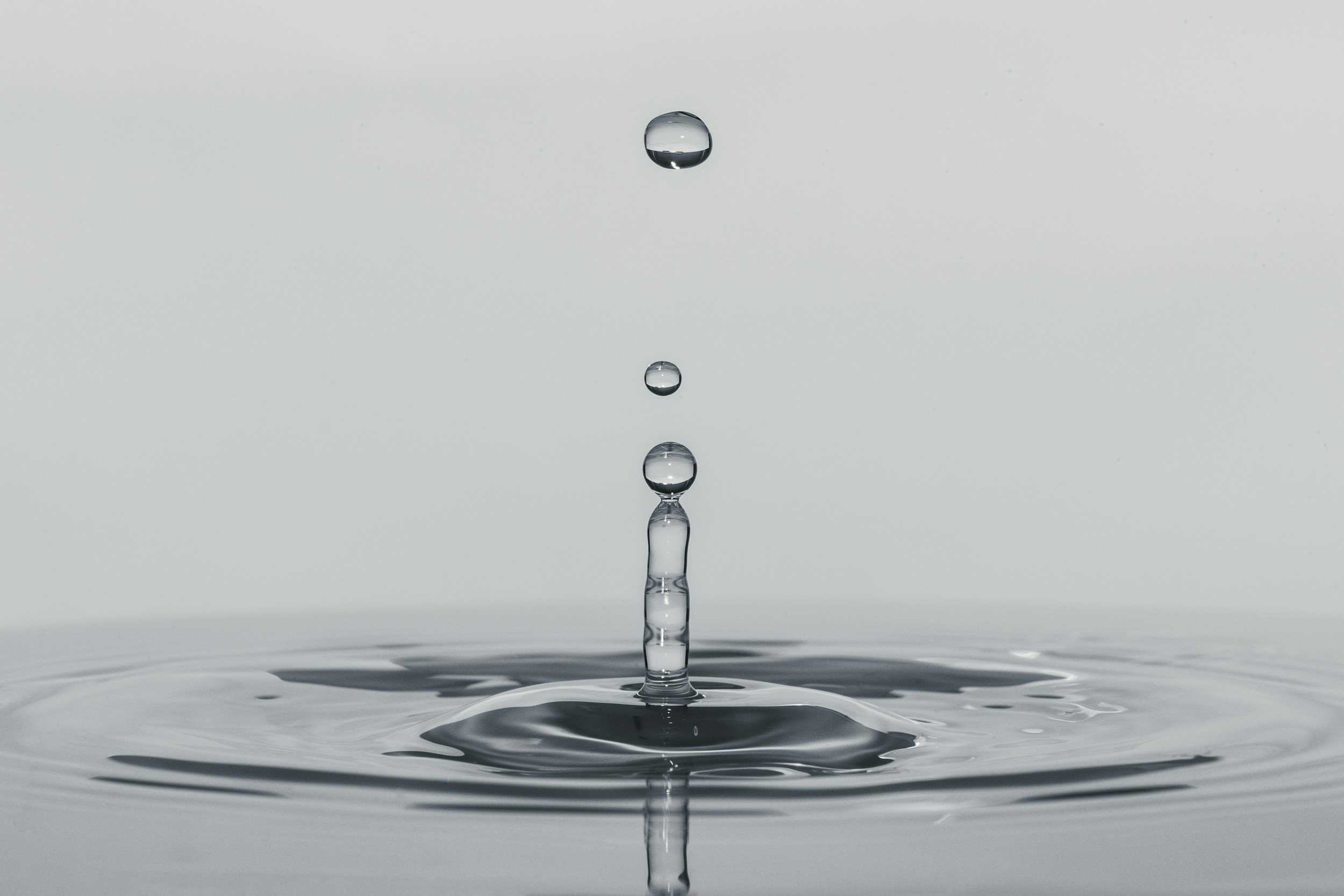 Close-up of water droplet hitting a calm water surface, creating a vertical column and smaller droplets