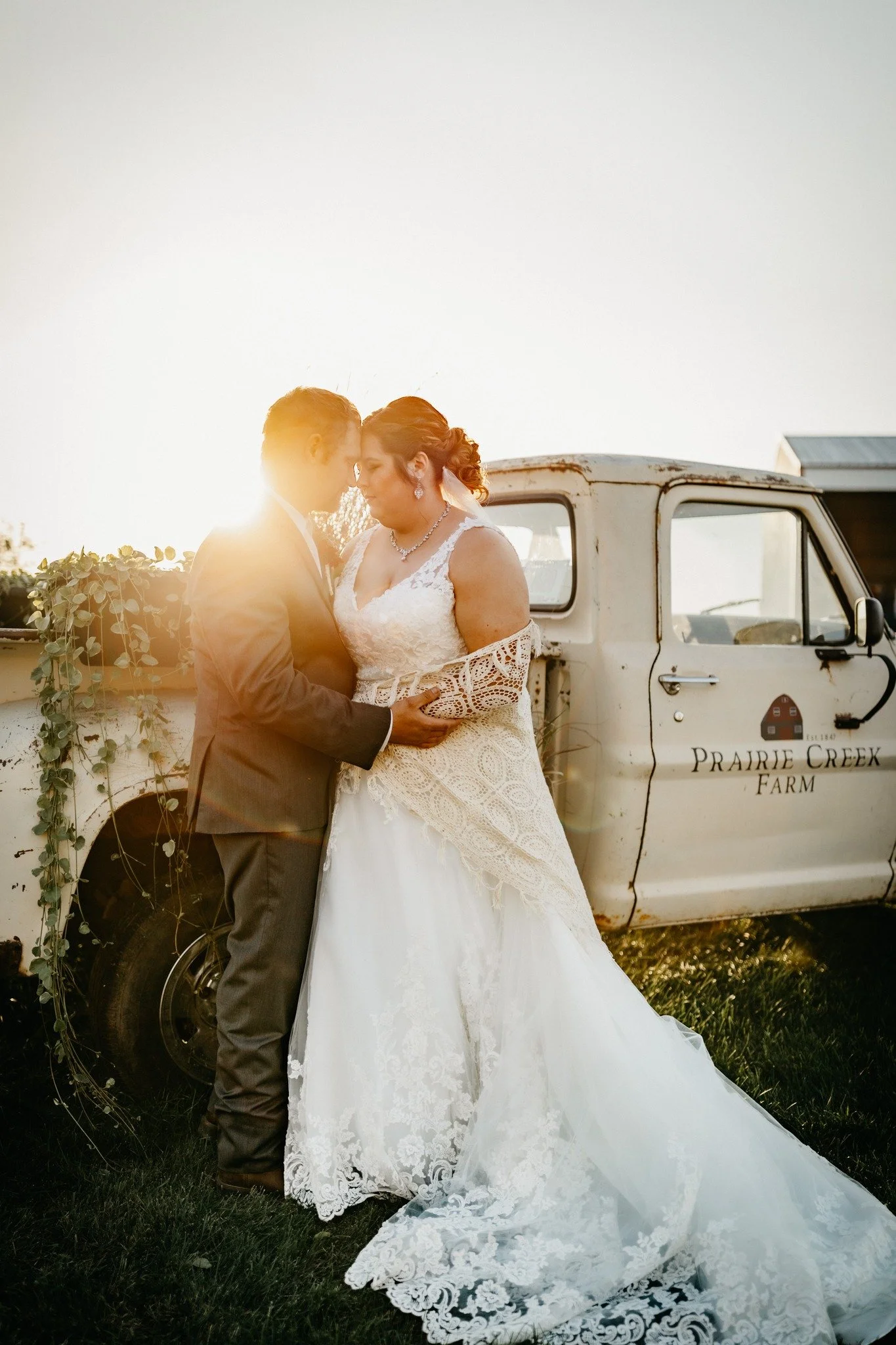 A bride and groom standing close together in front of an old truck during sunset, sharing an intimate moment.
