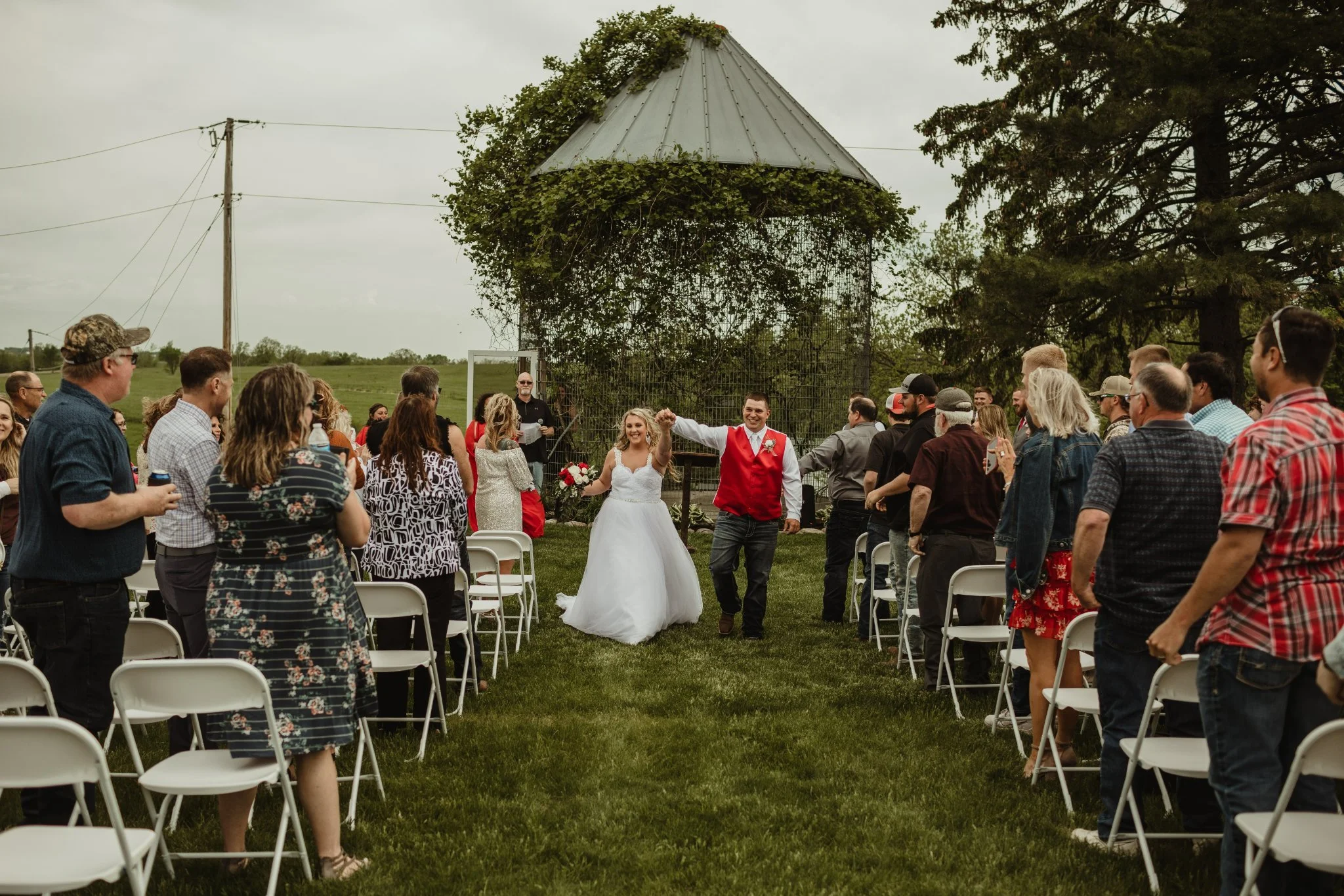 Bride and groom walking down the aisle after their wedding ceremony outdoors, surrounded by seated guests.