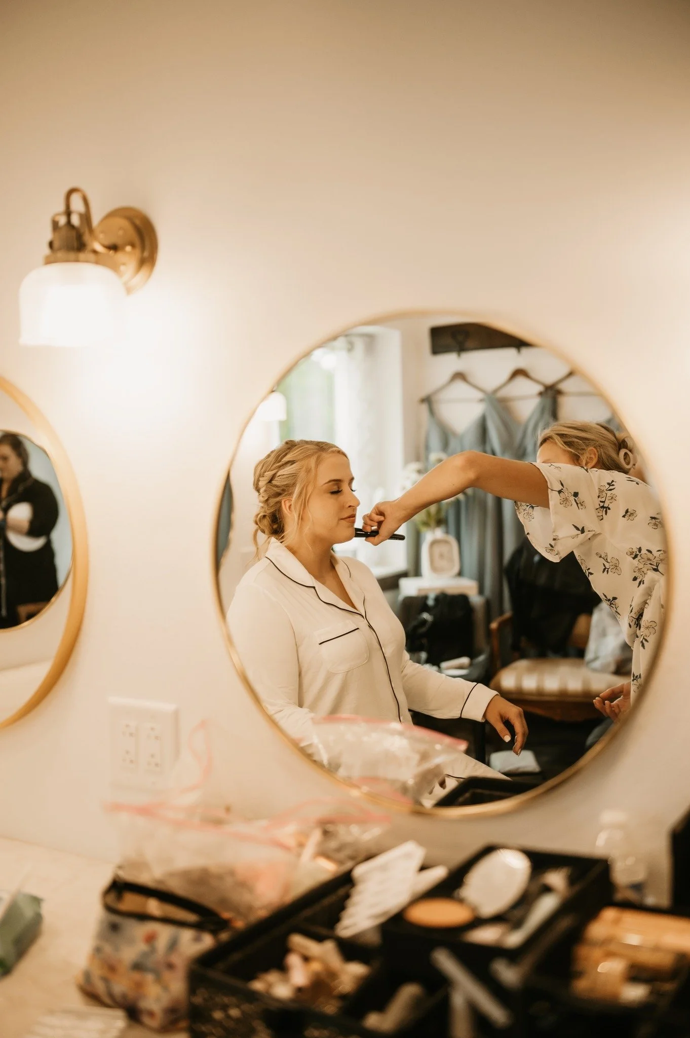 A woman getting her makeup done by a makeup artist in a room with a vanity mirror.