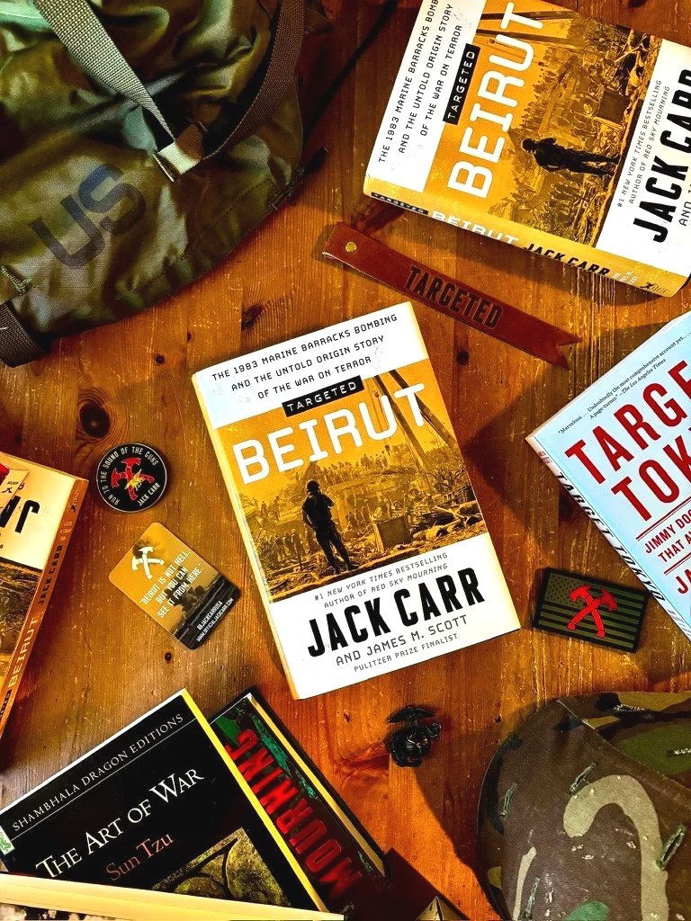 Books about Beirut and the war, a camouflage backpack, patches, and a target list on a wooden surface.