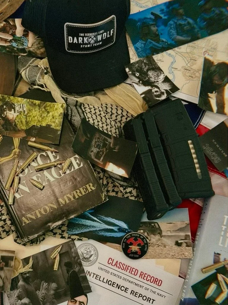 A collection of items including a black cap with a patch that says 'Dark Wolf,' photographs, a black gun magazine, a box of Winchester bullets, a classified record card, a black pin with a red skull logo, and various papers.