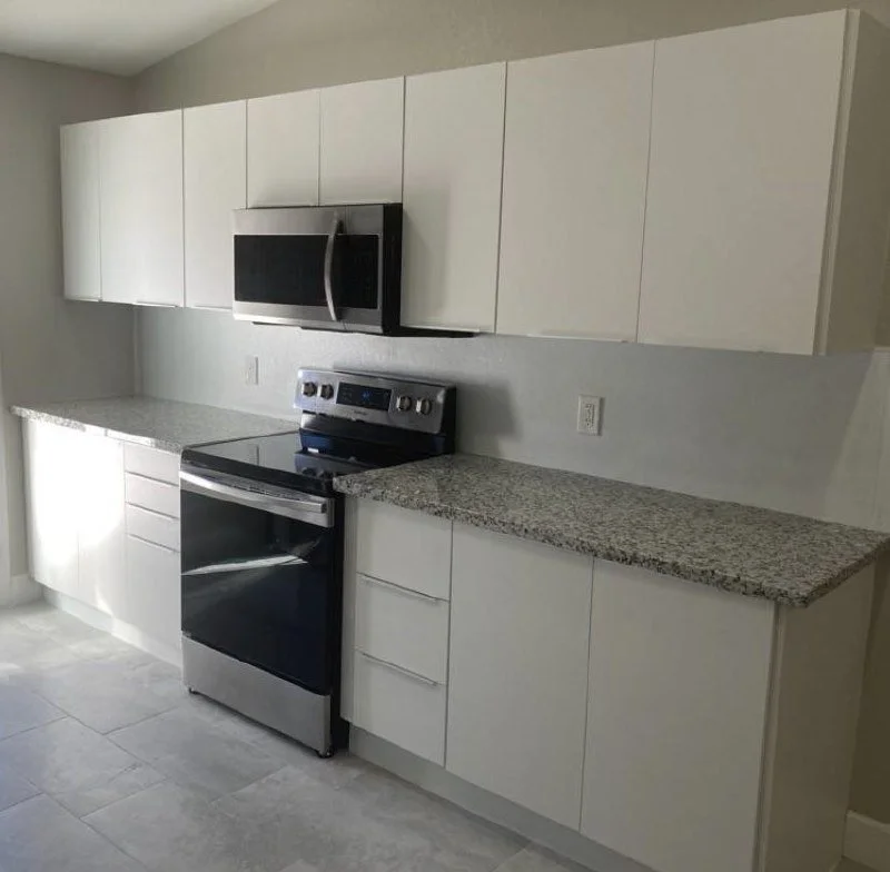 Kitchen with white cabinets, gray granite countertops, black and stainless steel stove, and black microwave
