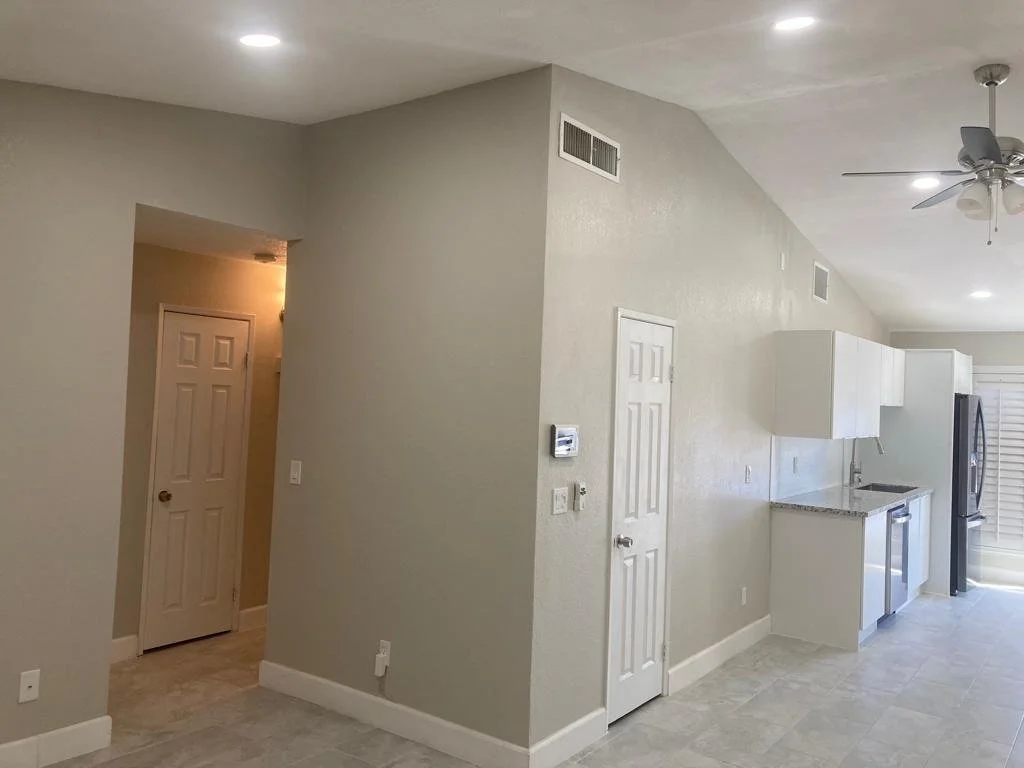 Empty kitchen with white cabinets, granite countertops, stainless steel appliances, a ceiling fan, and a door leading outside.