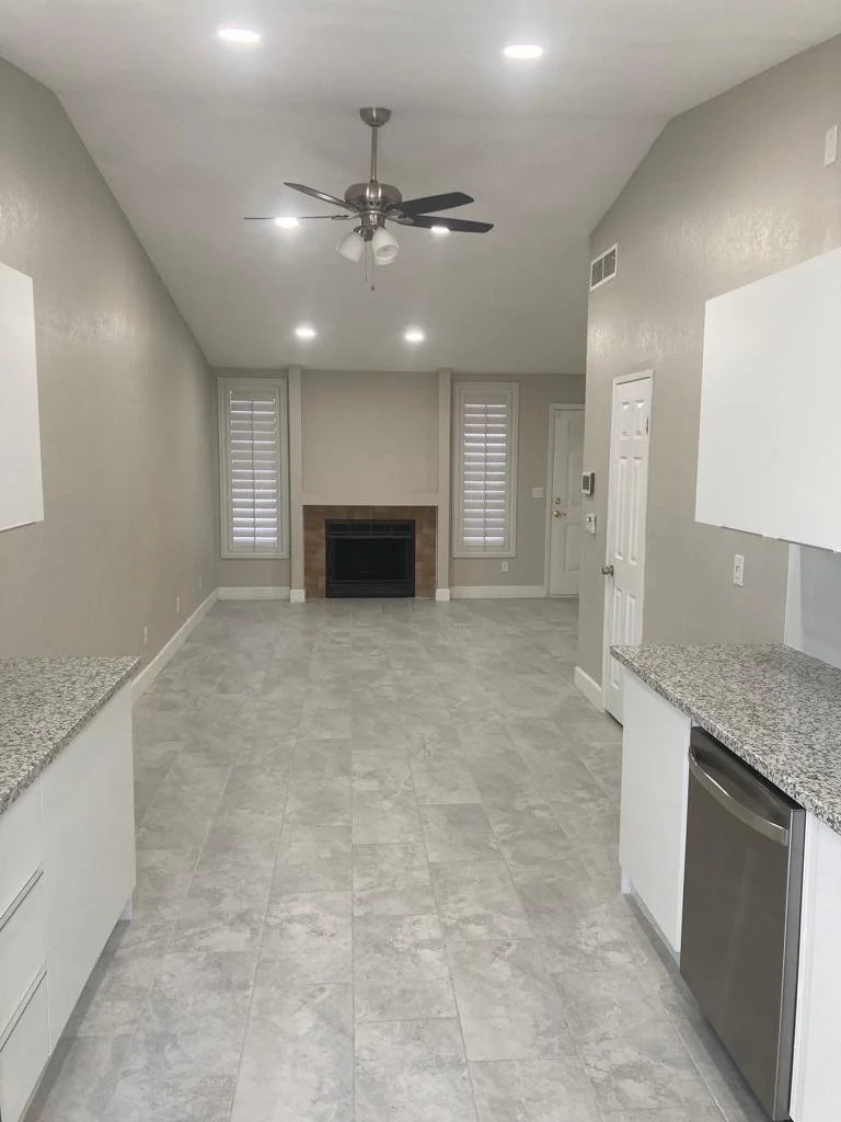 Empty living room with gray walls, light-colored tile flooring, a fireplace between two windows with blinds, and a ceiling fan with lights