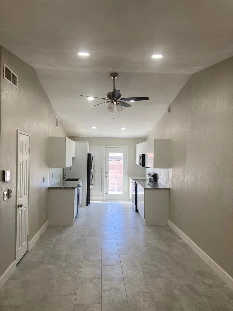 Empty kitchen with gray tiled floor, white cabinets, black refrigerator, black stove, microwave, ceiling fan with lights, and a door leading outside.