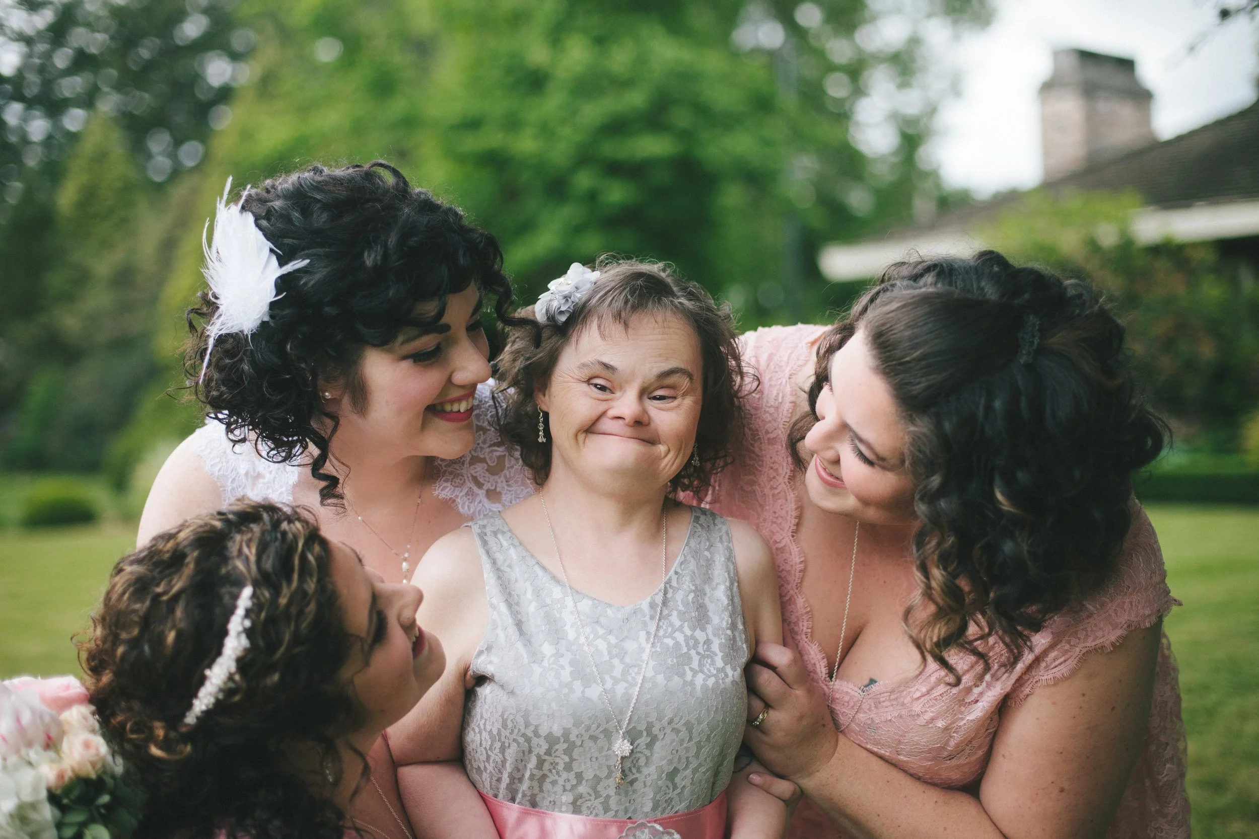 Four women and a girl smiling and hugging outdoors in a garden.