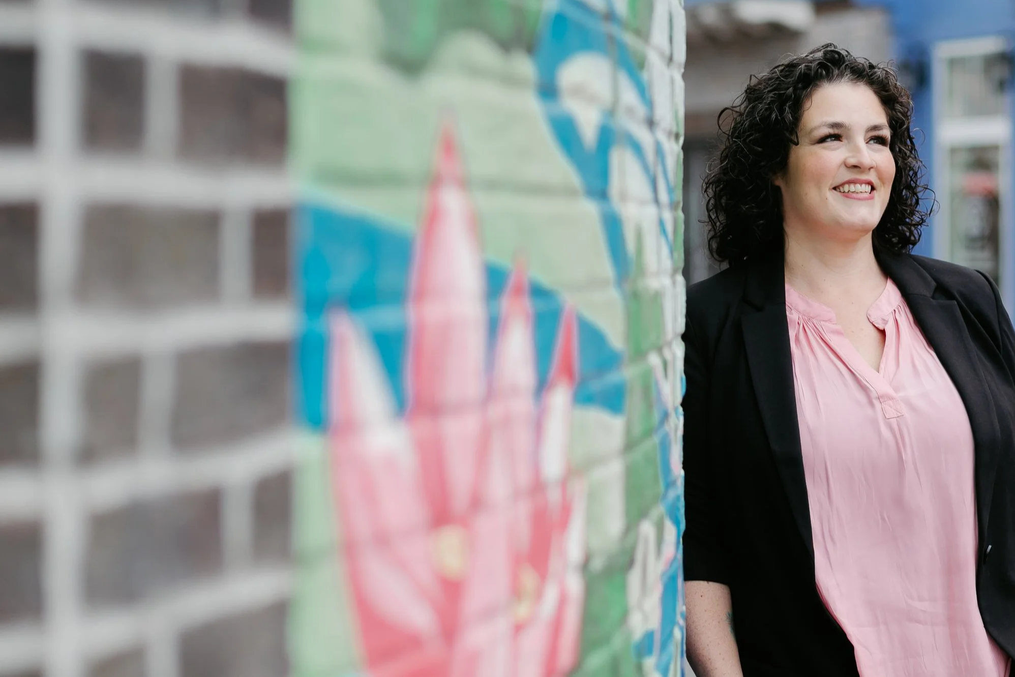 A woman smiling and standing next to a brick wall with colorful graffiti.