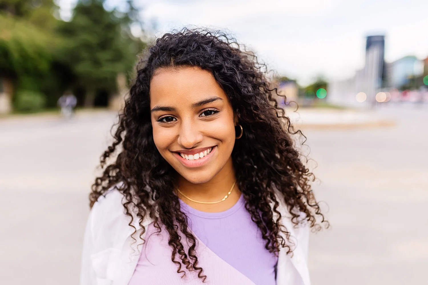 Happy young hispanic girl smiling, on a city street. Outside, joyful teen over urban background.