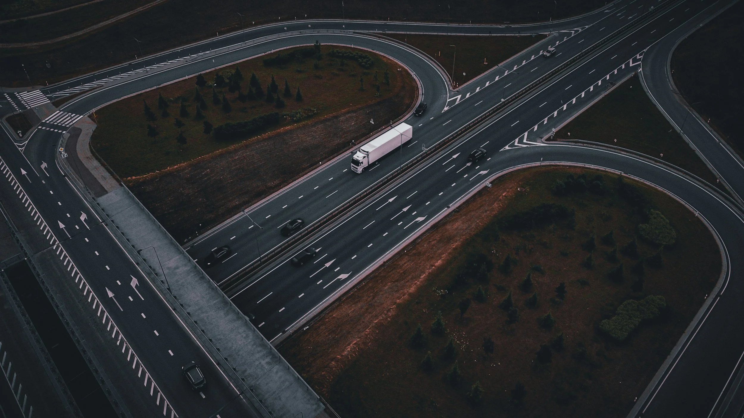 Aerial view of a multi-level highway interchange with several curved ramps and roads, some with vehicles, and green landscaping in the center area.