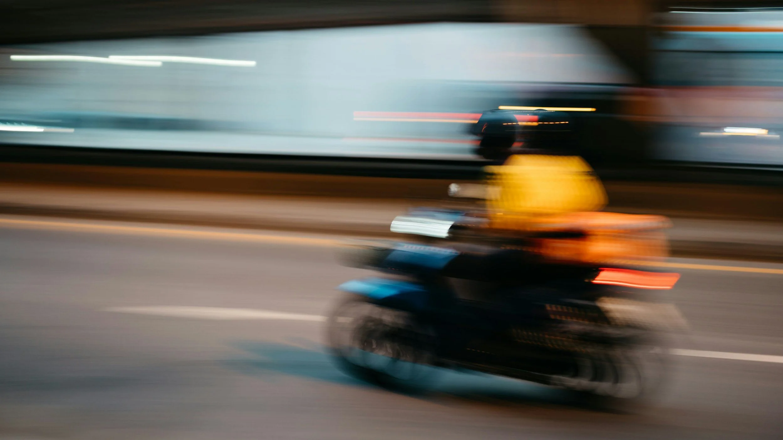 Blurred motion photo of a motorcycle riding on a road at night with streaks of lights in the background.