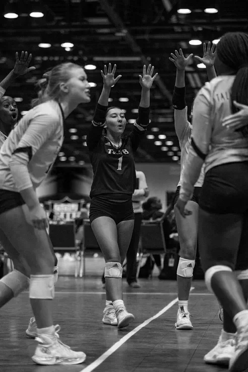 Volleyball players on court celebrating with high-fives in an indoor arena.
