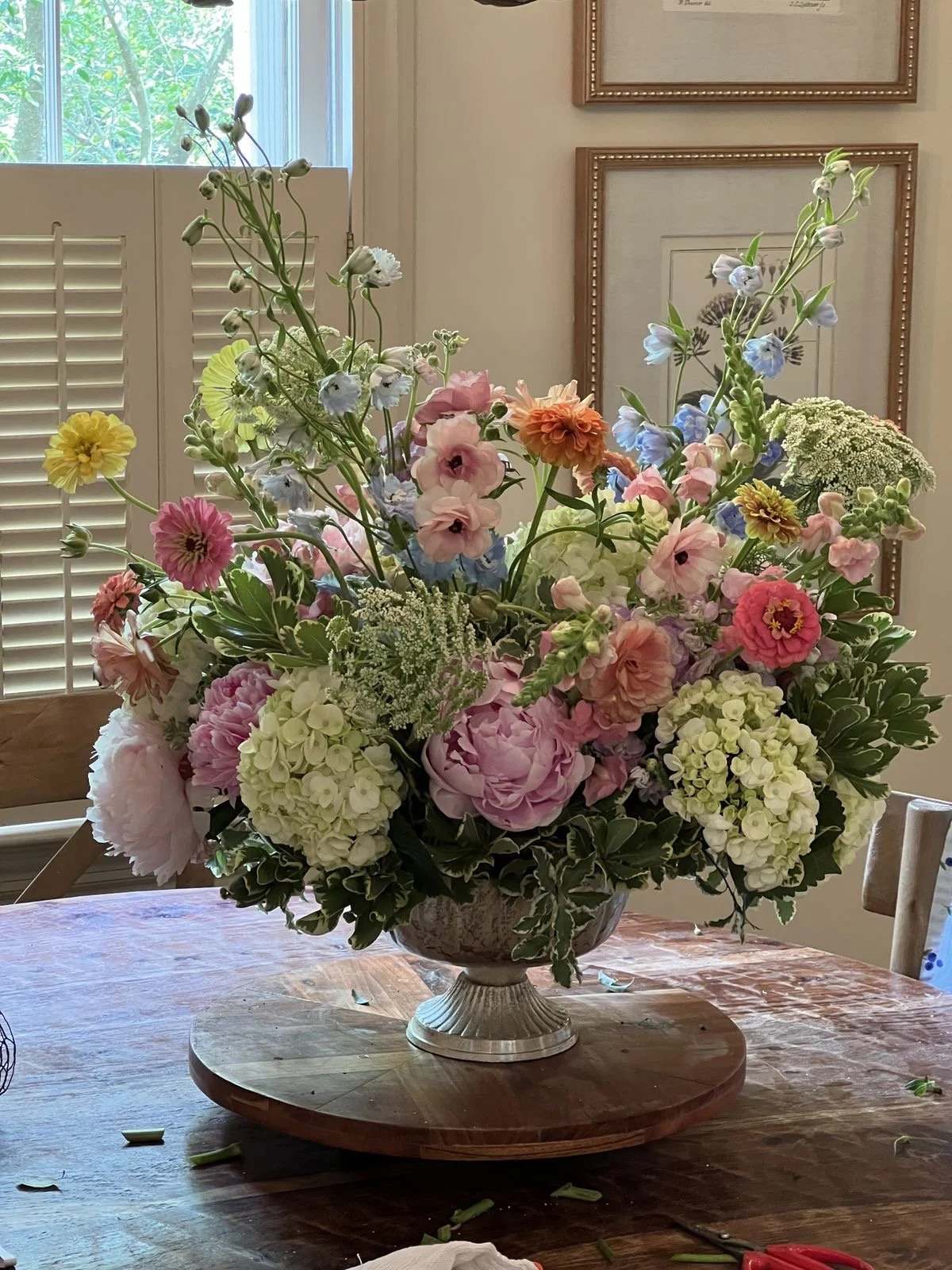A large bouquet of assorted pastel-colored flowers in a decorative vase on a wooden table.