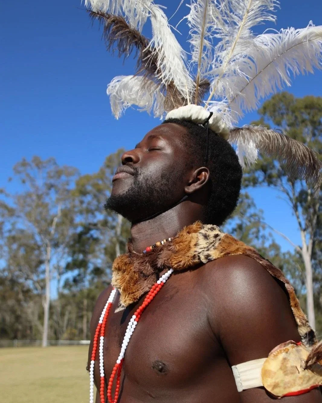 A man with dreadlocks wearing a colorful, patterned blazer speaking into a microphone at an event.