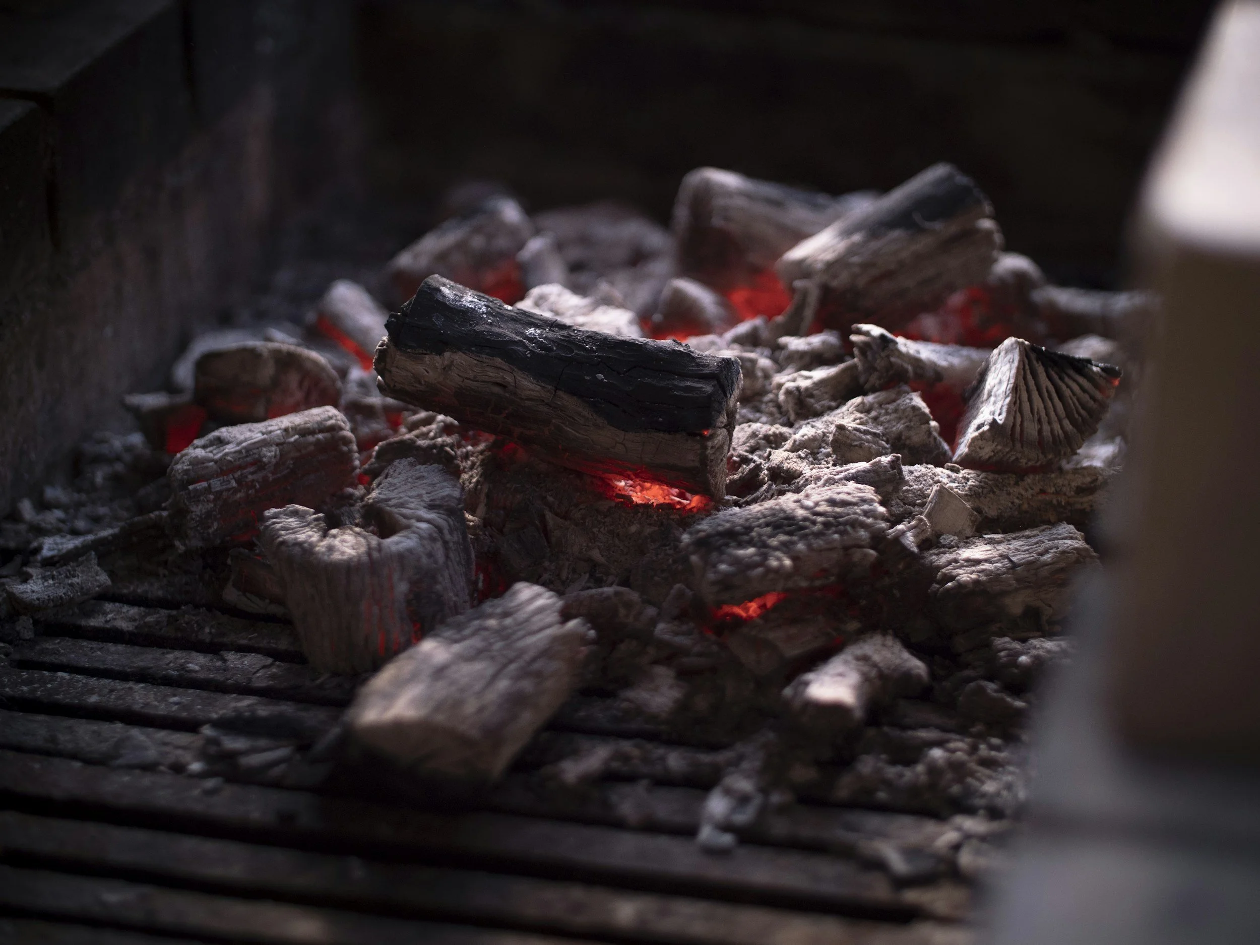 Close-up of burning charcoal with glowing embers and ash on a grill.