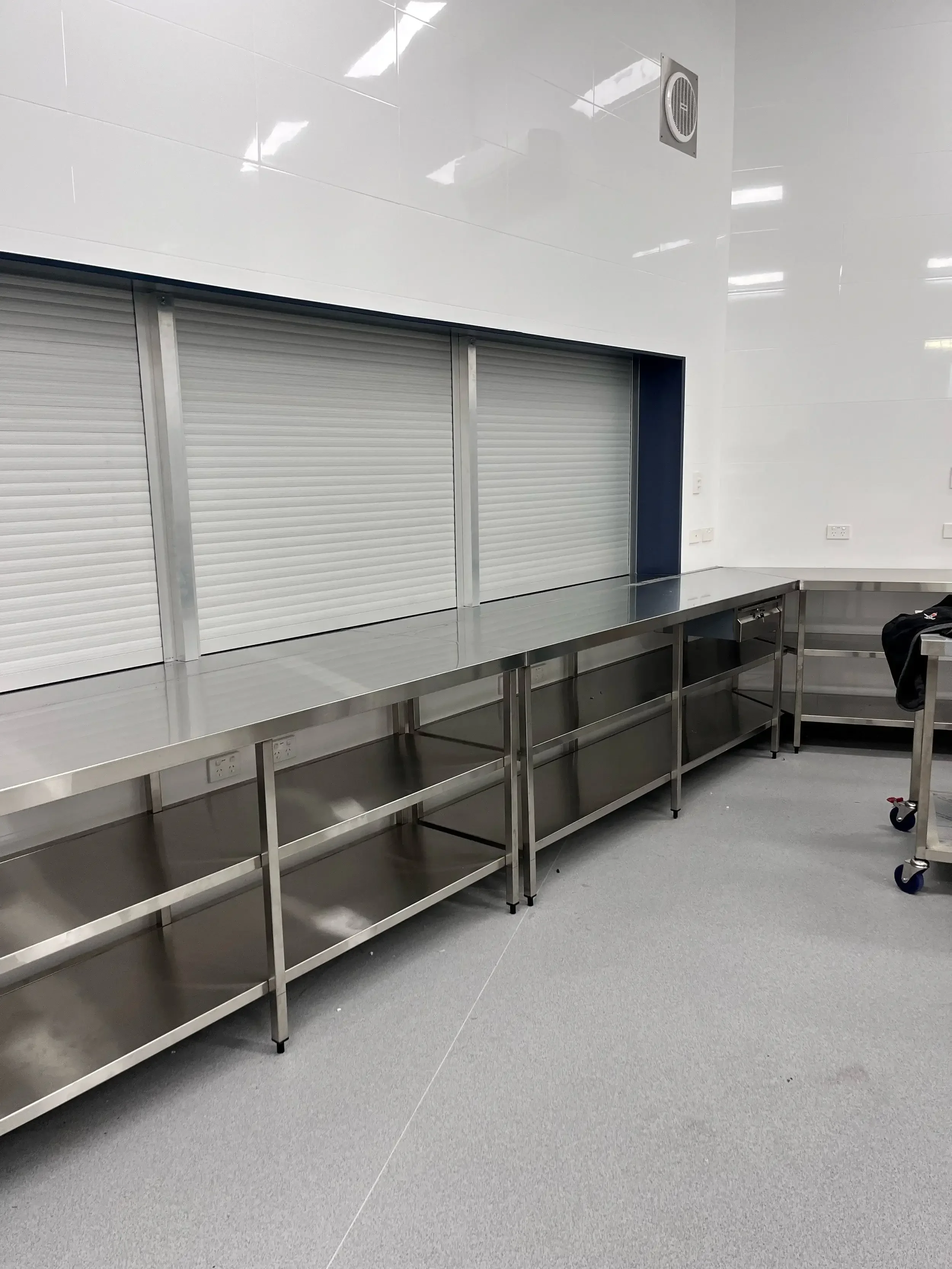Empty stainless steel countertop and shelving in a commercial kitchen, with a white rolling shutter in the background.