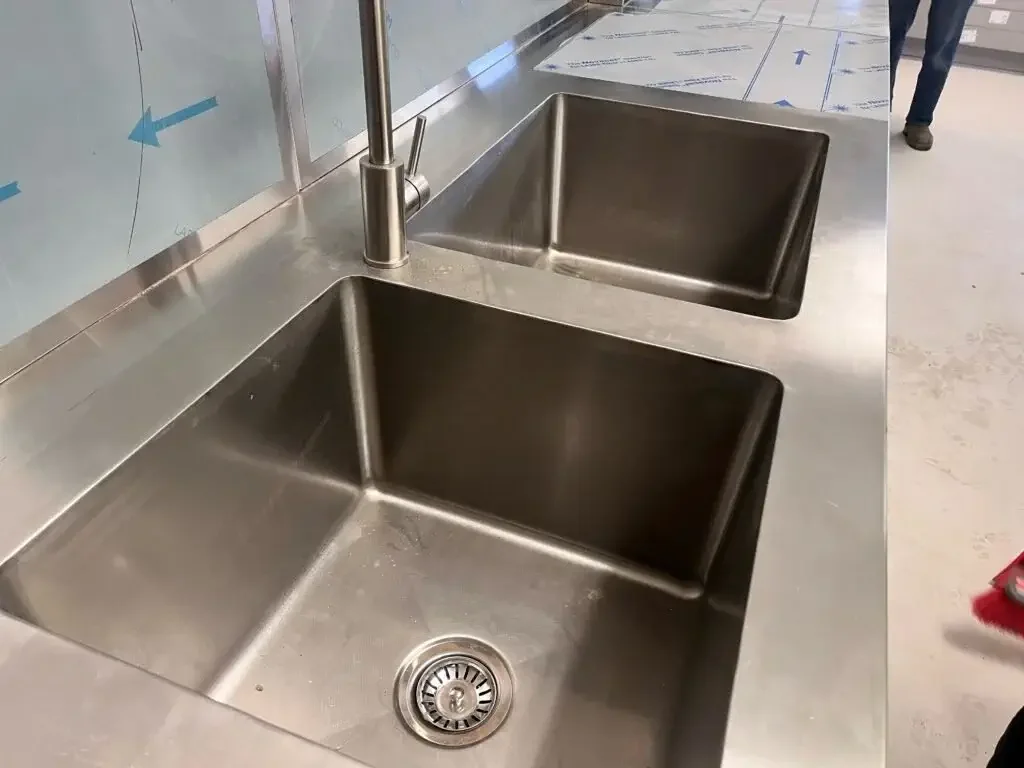 Stainless steel double kitchen sink with a faucet, in a commercial or industrial setting.
