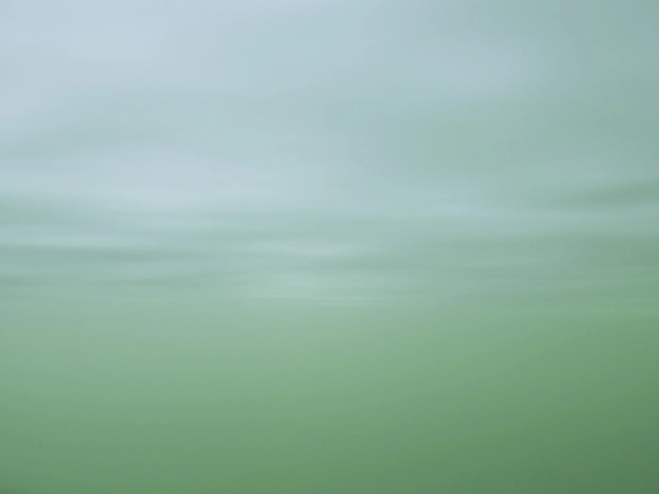Blurry green and blue abstract background, resembling a landscape or sky scene.